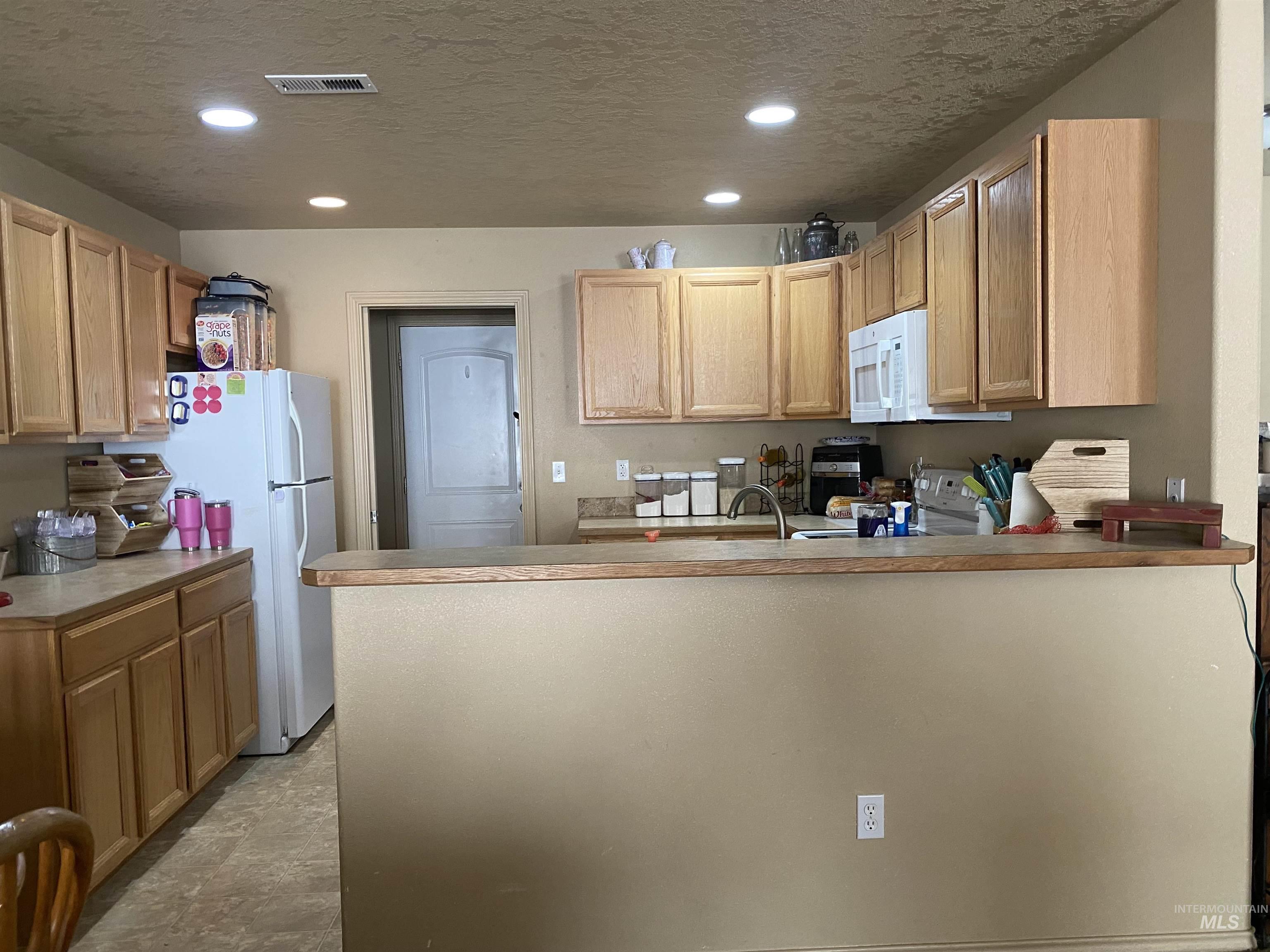 Kitchen featuring a textured ceiling, light countertops, recessed lighting, a peninsula, and white appliances