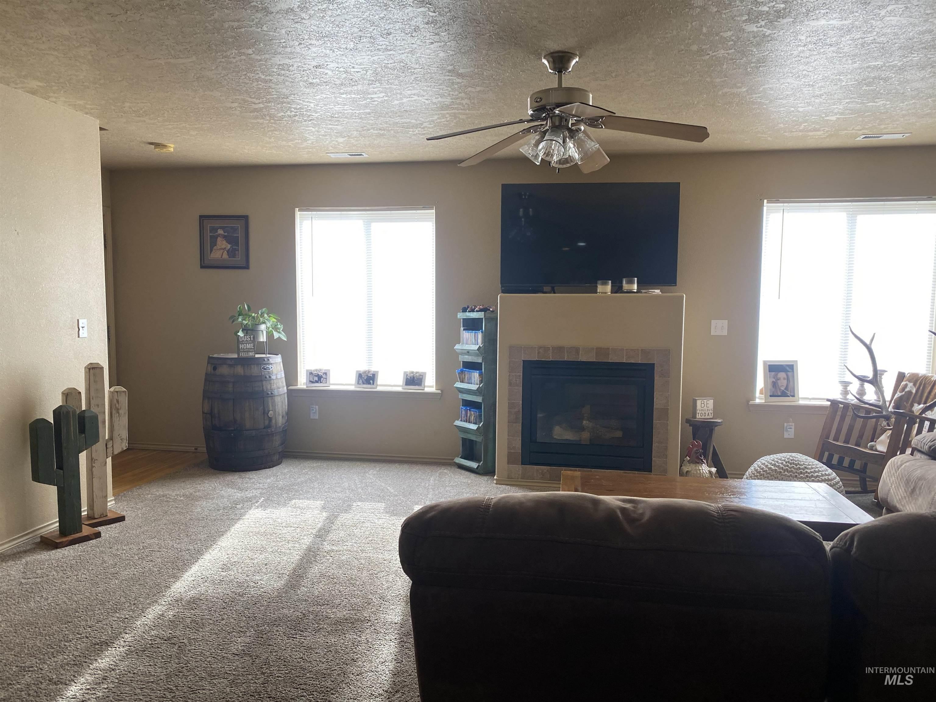 Living area with a textured ceiling, a tiled fireplace, ceiling fan, and carpet floors