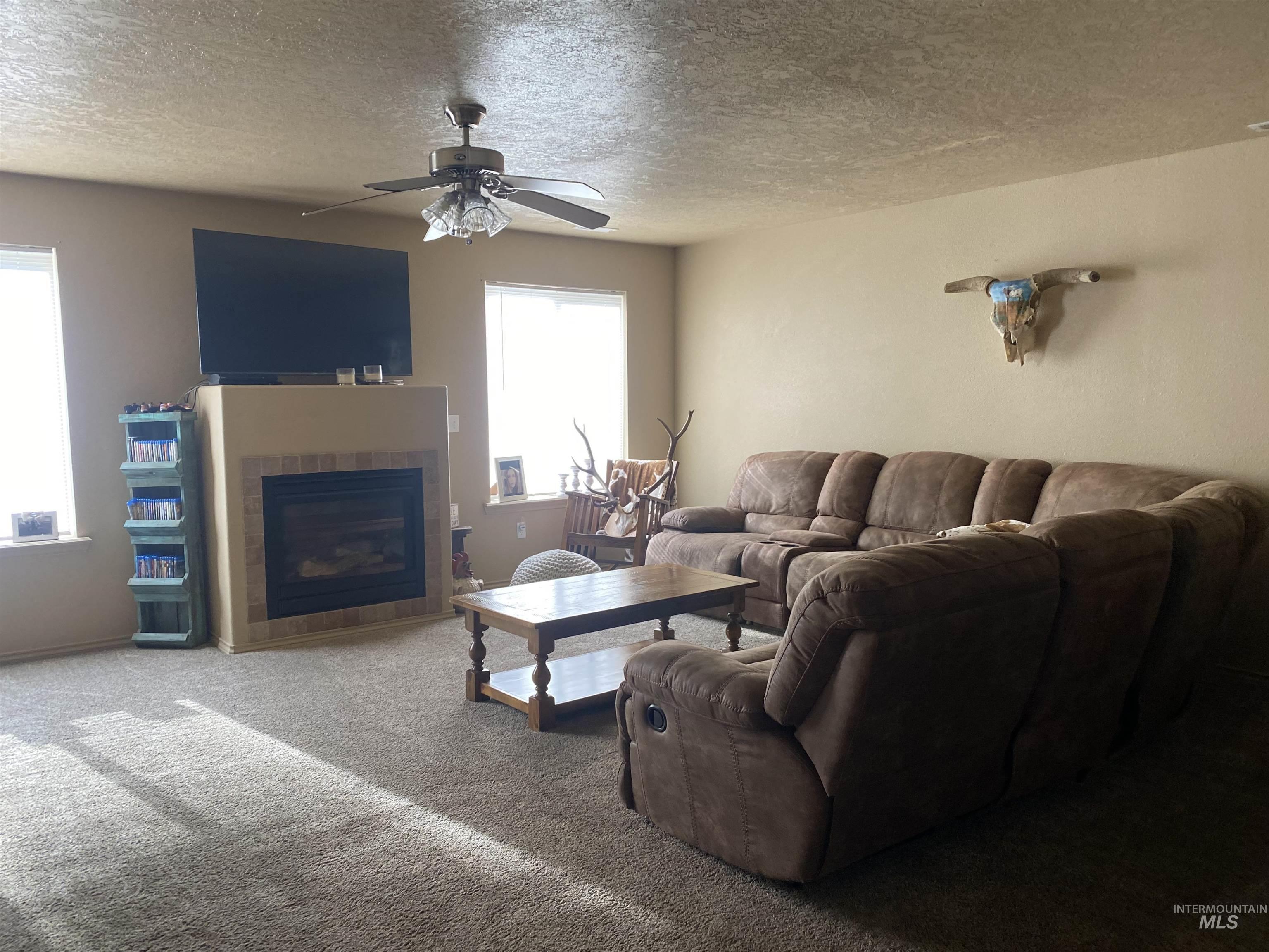 Carpeted living room featuring a fireplace, a textured ceiling, and a ceiling fan