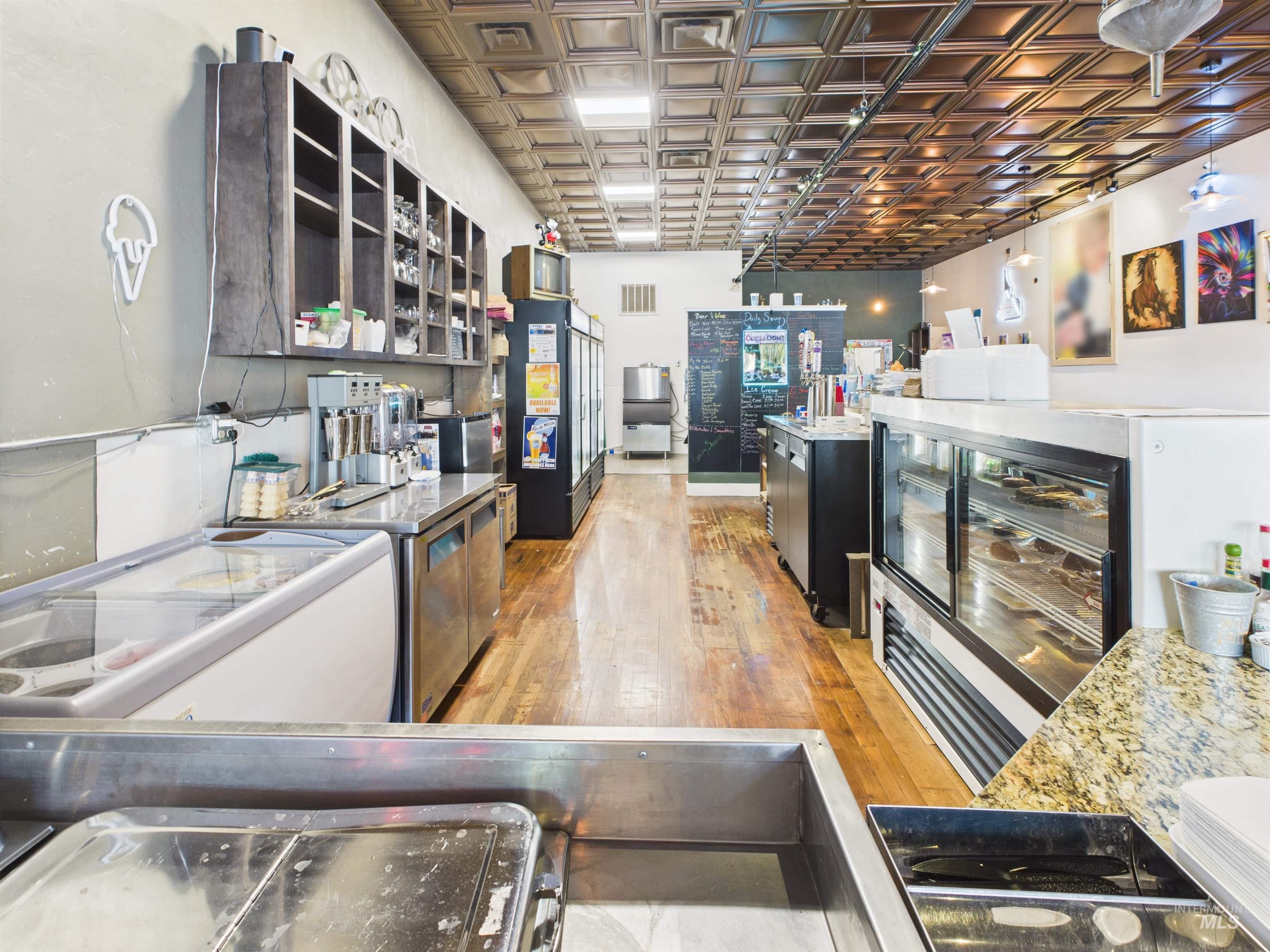Kitchen with light wood-type flooring, an ornate ceiling, freestanding refrigerator, light stone counters, and dark cabinetry