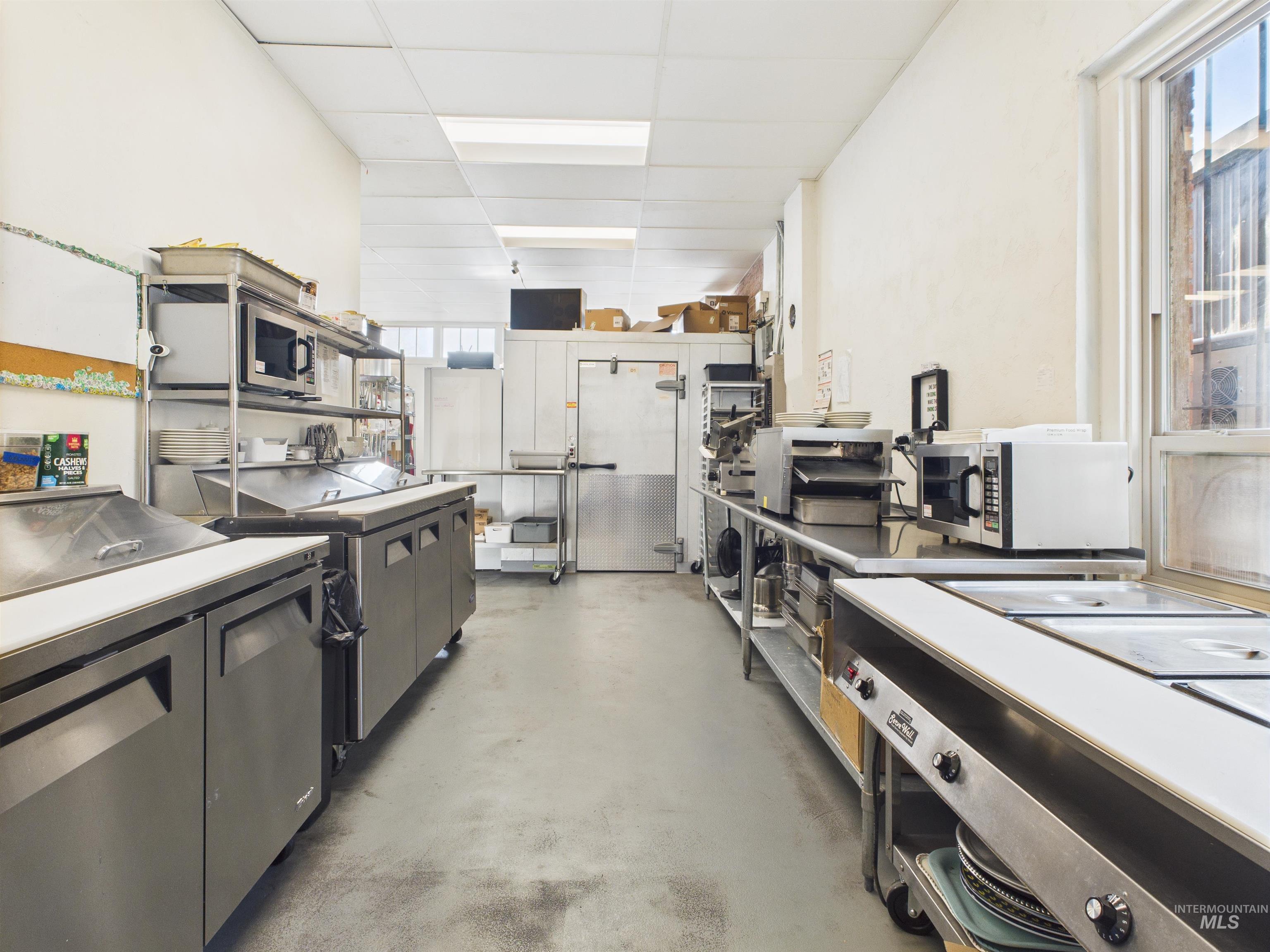 Kitchen featuring a paneled ceiling, open shelves, concrete floors, stainless steel microwave, and stainless steel countertops