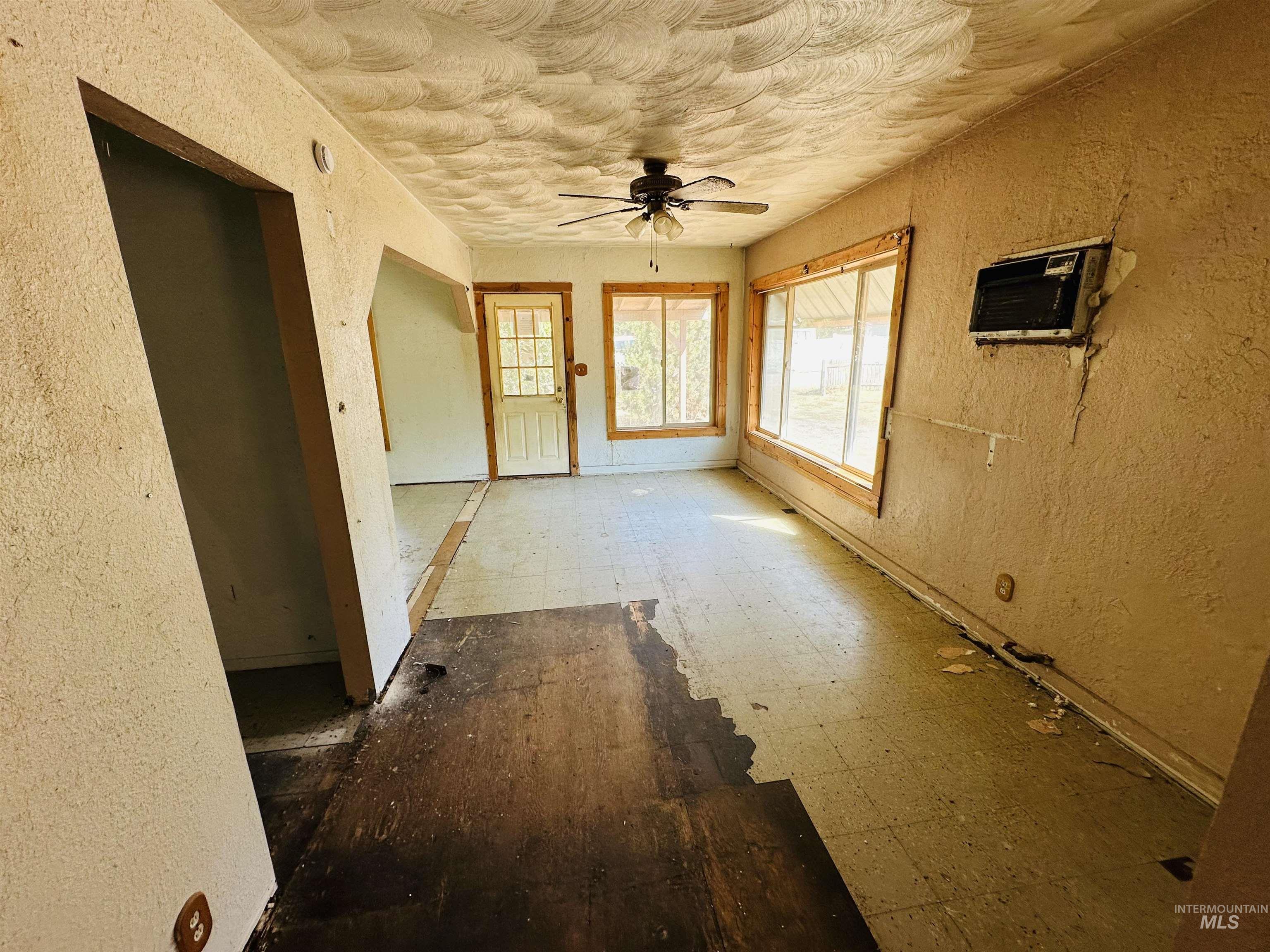 Empty room with a textured wall, a ceiling fan, and a wall mounted air conditioner