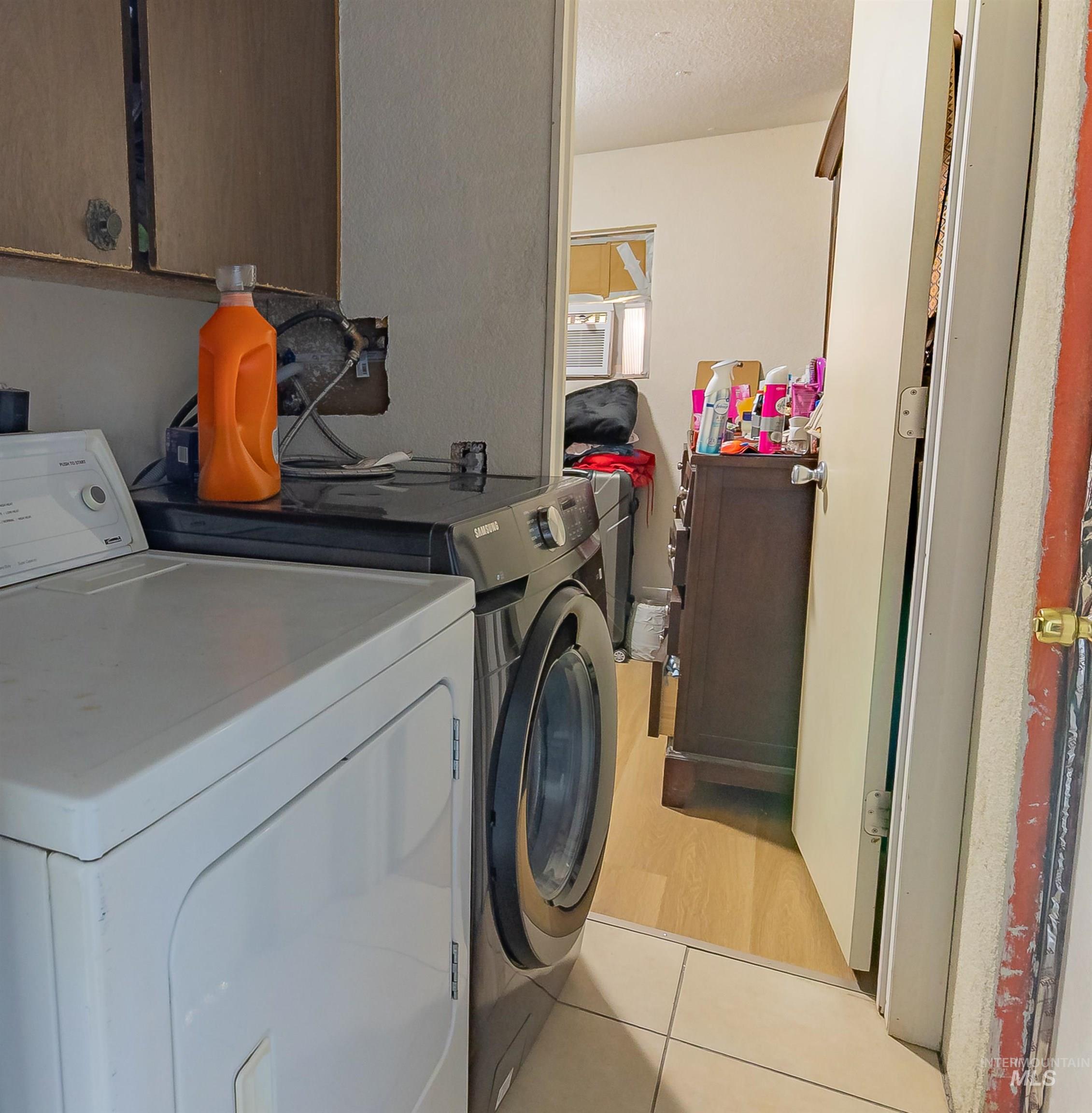 Washroom with light tile patterned flooring, cabinet space, washing machine and clothes dryer, and a textured ceiling