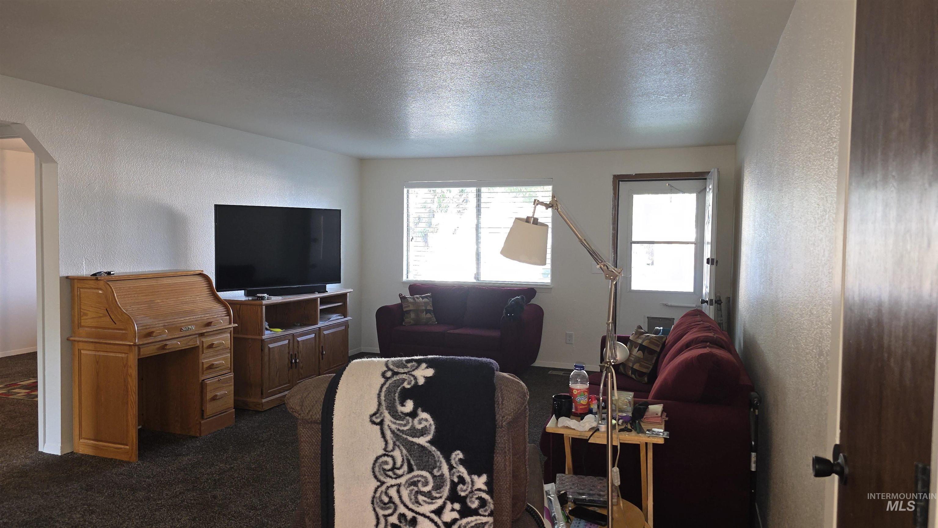 Living room with a textured wall, arched walkways, a textured ceiling, and dark carpet