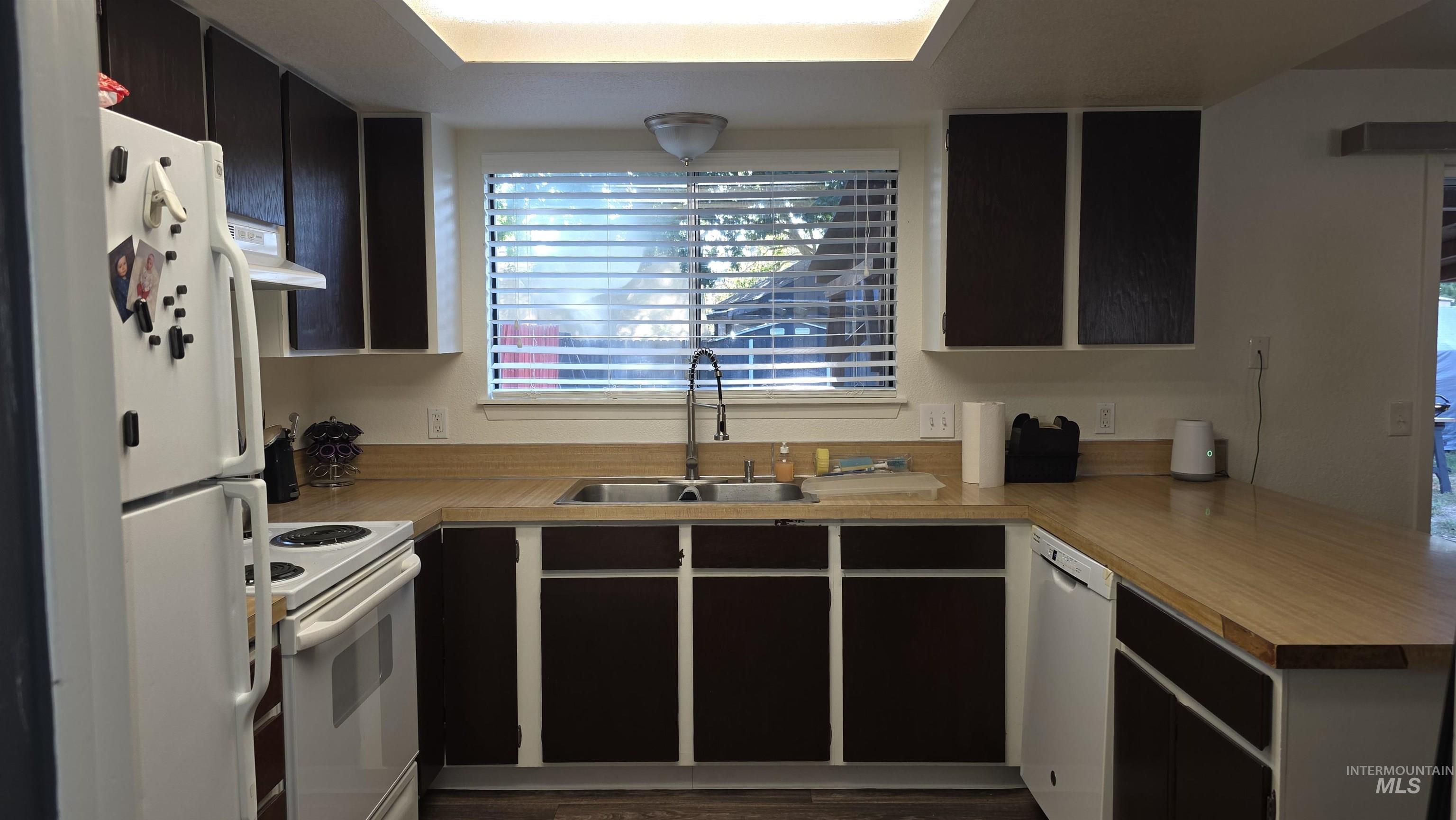 Kitchen featuring white appliances, light countertops, exhaust hood, and a peninsula