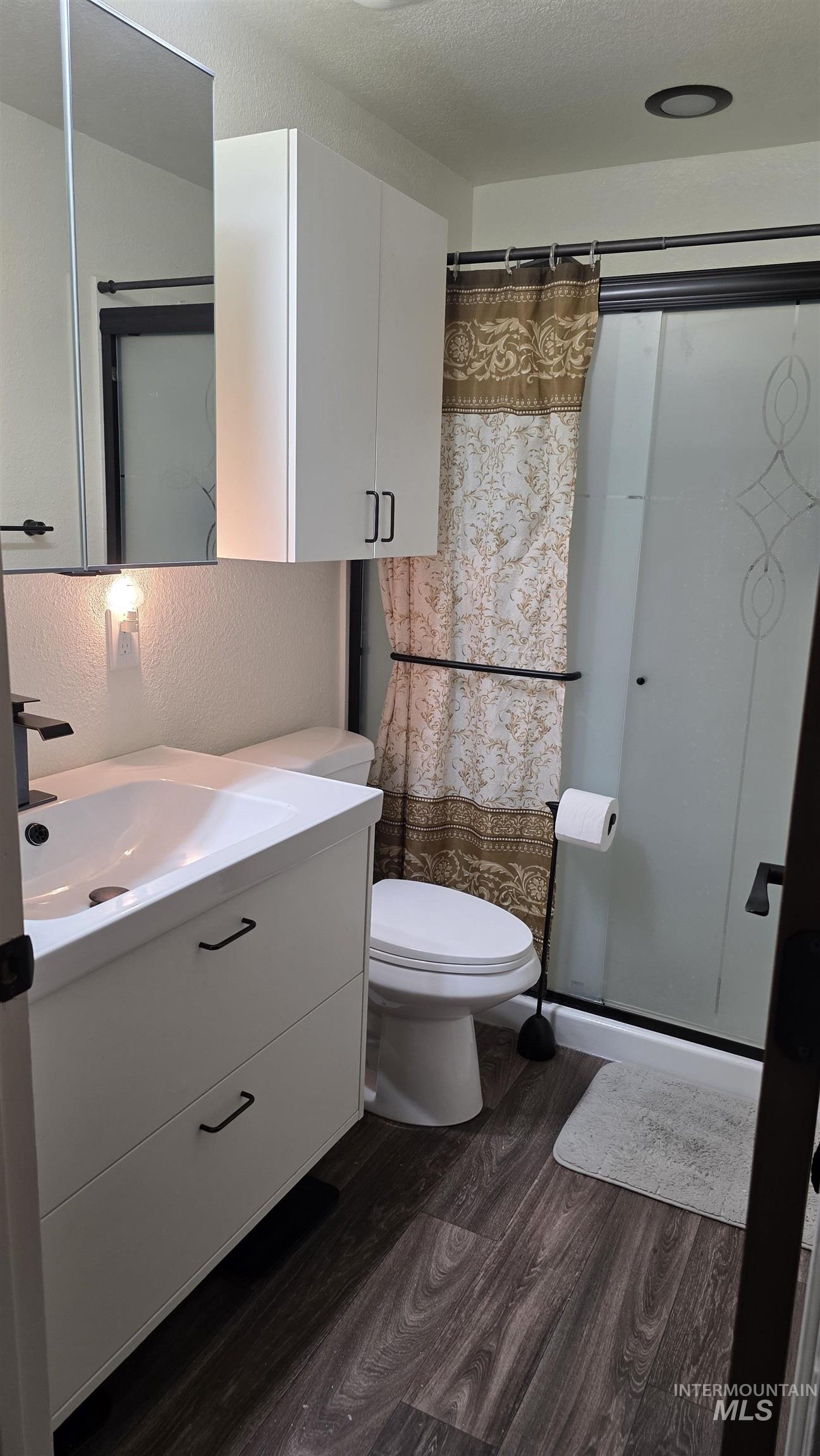 Full bathroom with dark wood-type flooring, vanity, a stall shower, a textured ceiling, and a textured wall