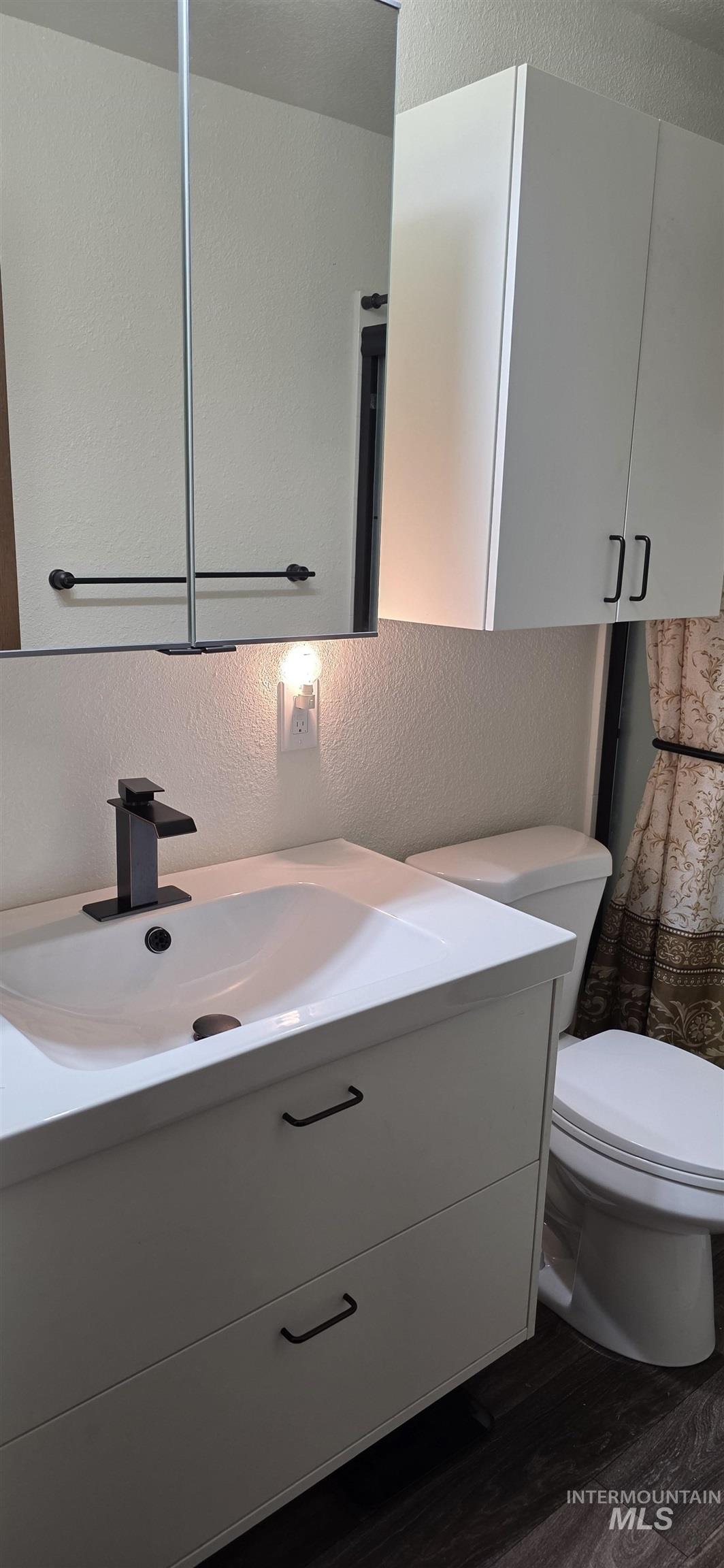 Bathroom featuring a textured wall, vanity, and dark wood-style floors