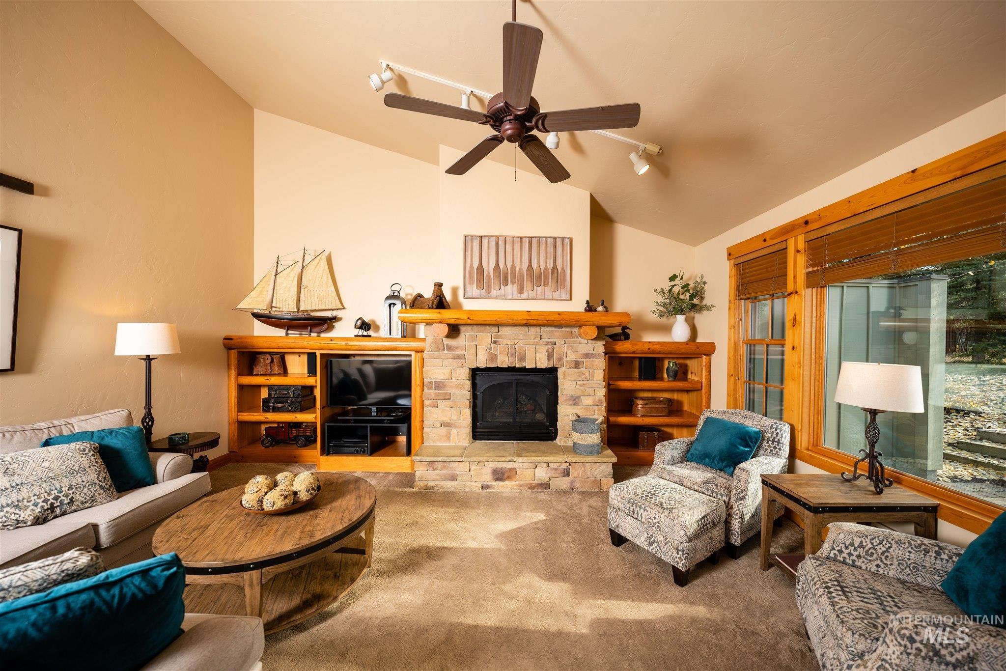 Carpeted living room with vaulted ceiling, a fireplace, and a ceiling fan