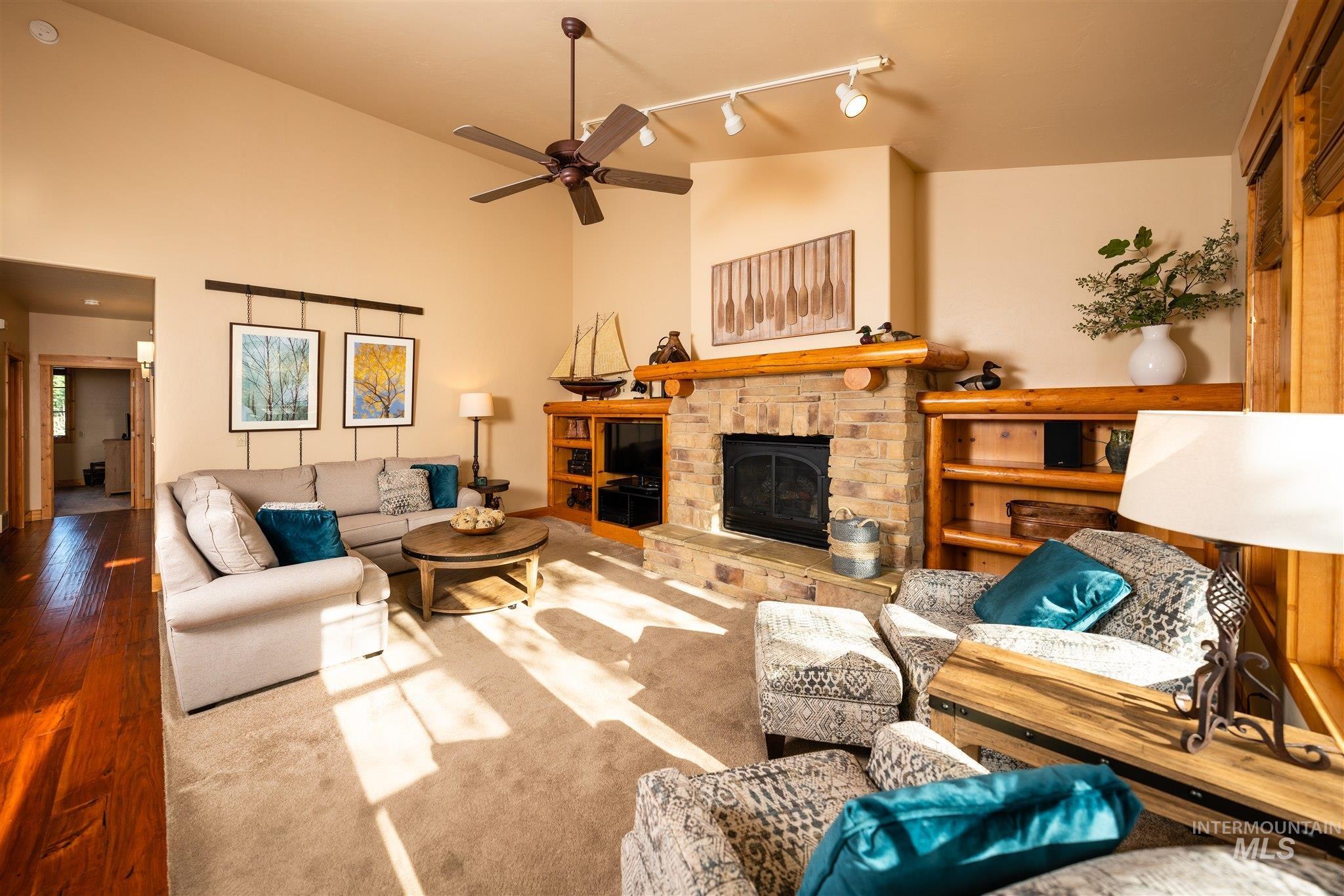 Living room with a fireplace, track lighting, hardwood / wood-style floors, a ceiling fan, and high vaulted ceiling