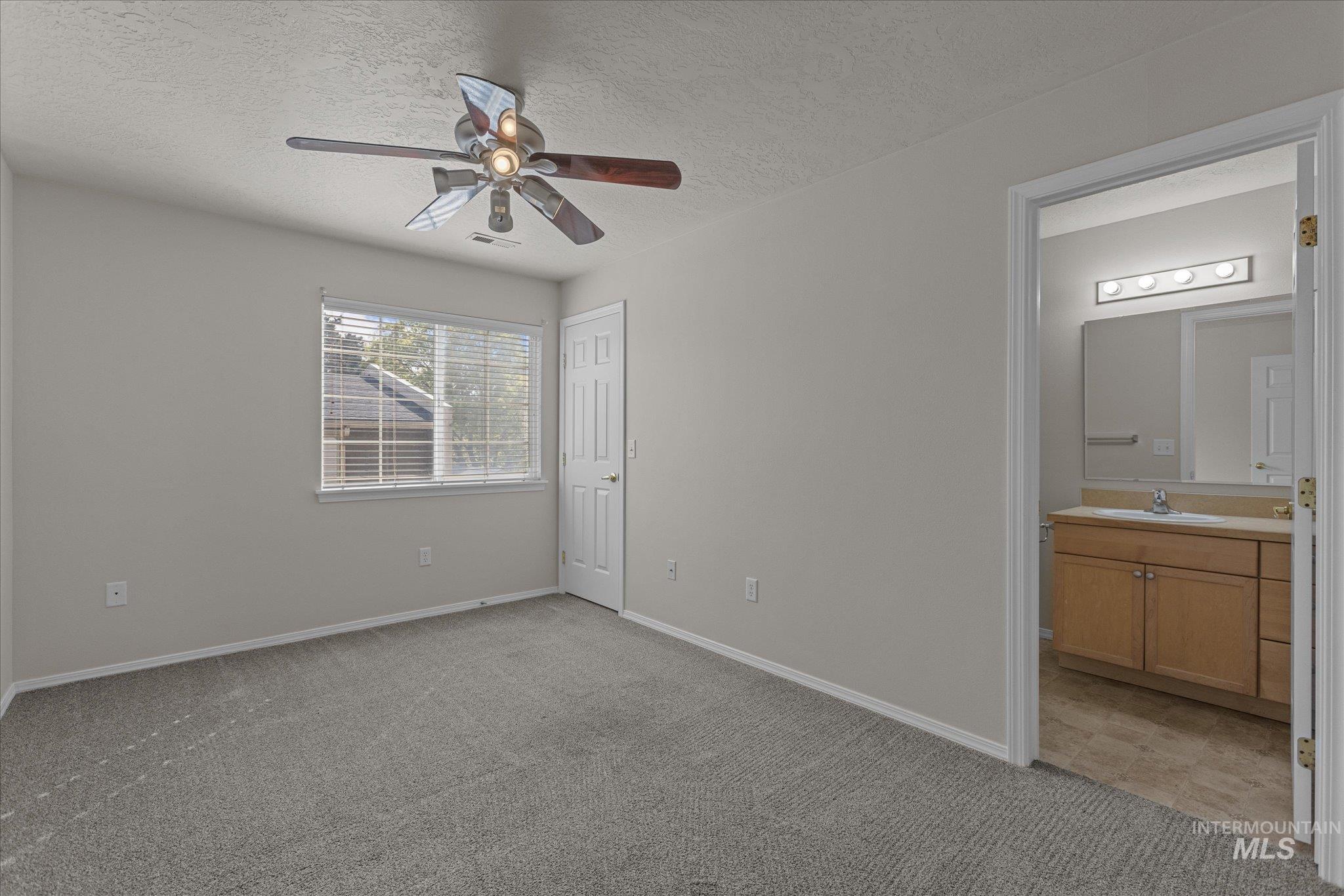 Unfurnished bedroom with a textured ceiling, light carpet, ensuite bath, and ceiling fan