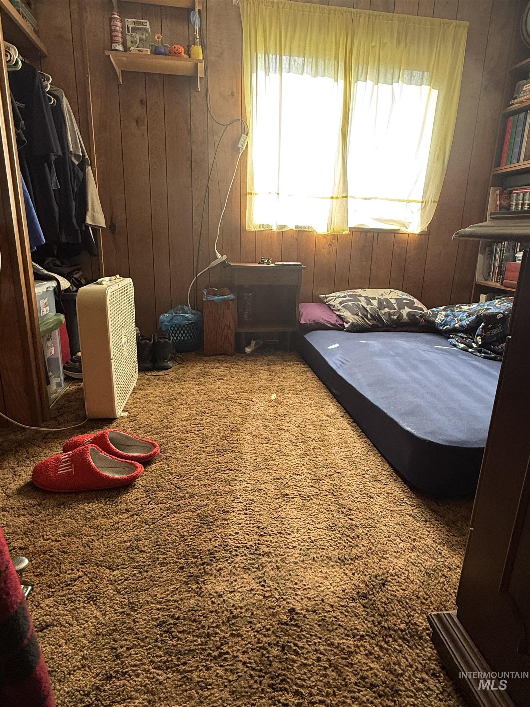 Bedroom with multiple windows, wooden walls, and carpet flooring