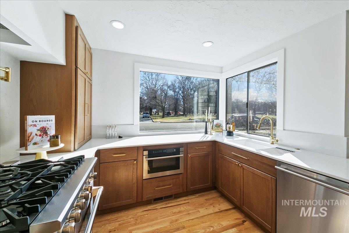 Kitchen with stainless steel appliances, light wood finished floors, brown cabinets, exhaust hood, and recessed lighting