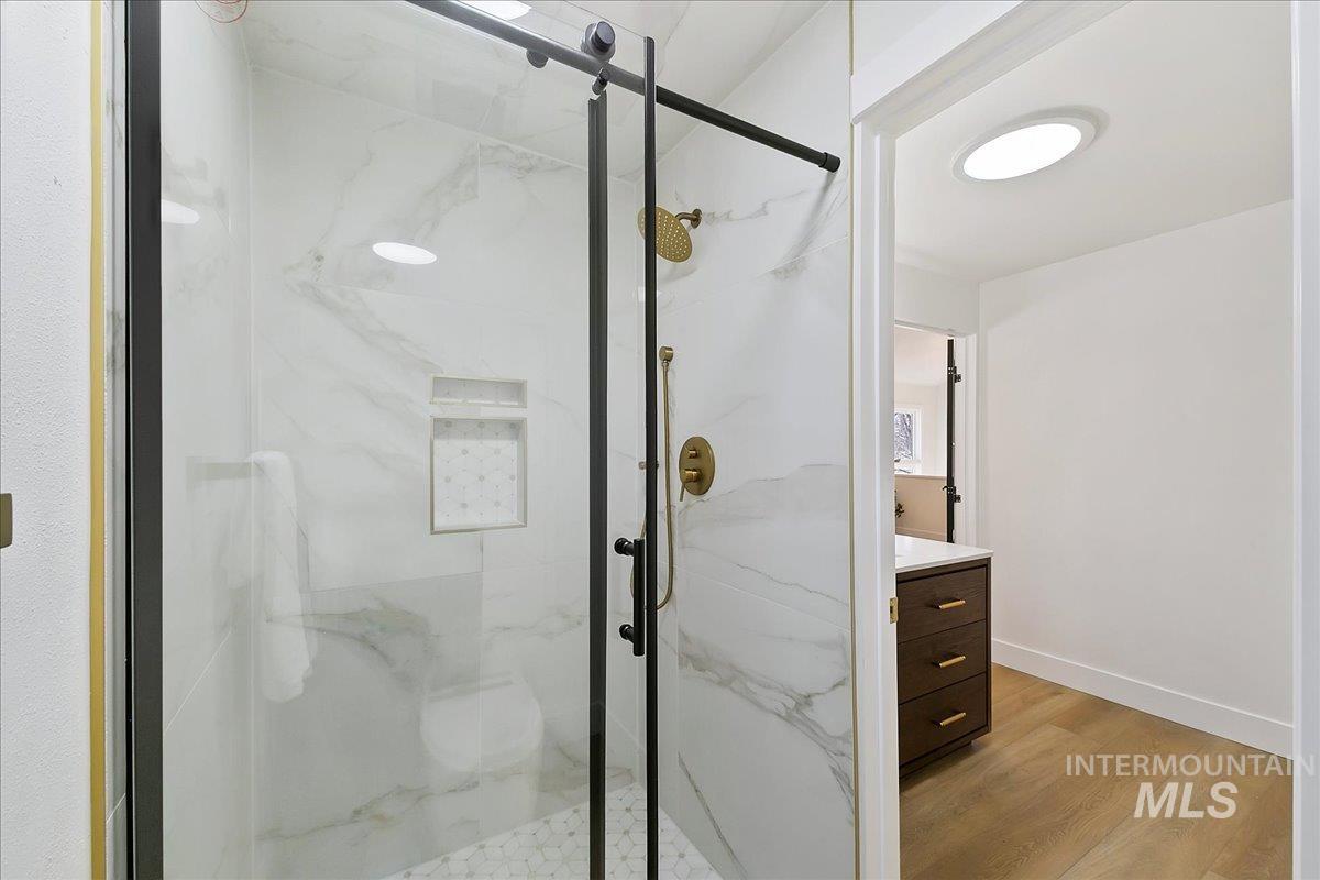 Full bathroom featuring a marble finish shower, vanity, and light wood-style flooring