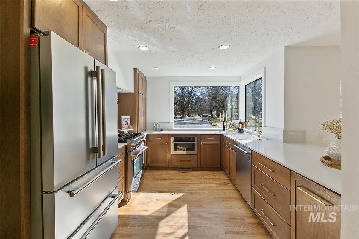 Kitchen featuring brown cabinets, high quality appliances, light wood-style floors, a textured ceiling, and recessed lighting