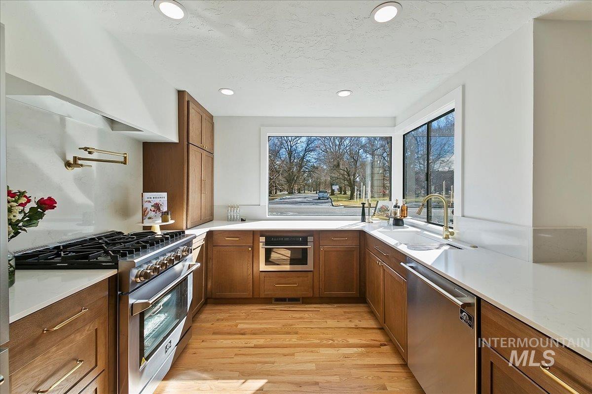Kitchen featuring brown cabinets, stainless steel appliances, light wood finished floors, recessed lighting, and light stone counters