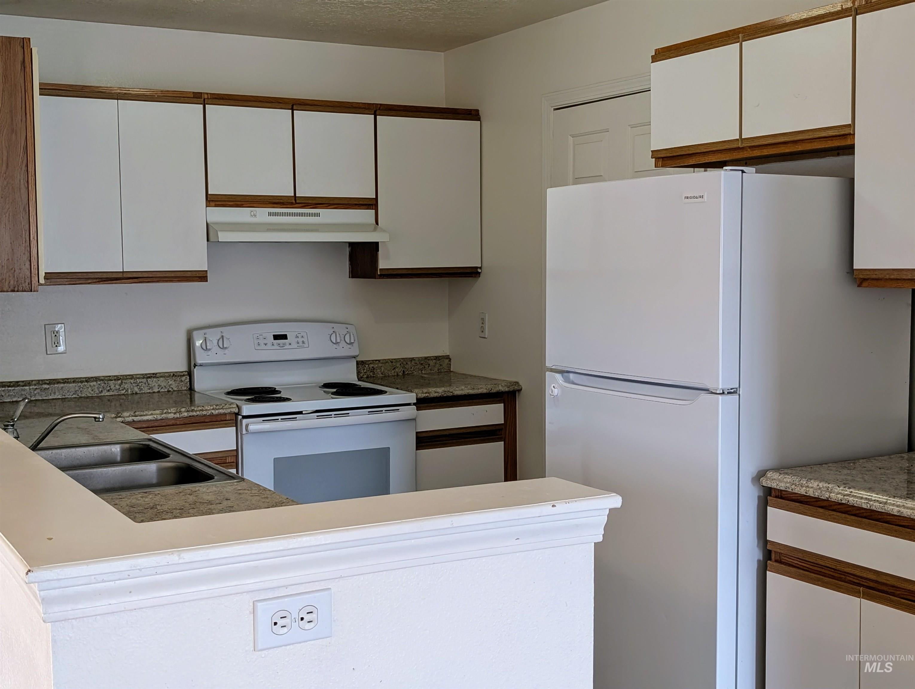 Kitchen with white cabinets, white appliances, a peninsula, under cabinet range hood, and brown cabinetry