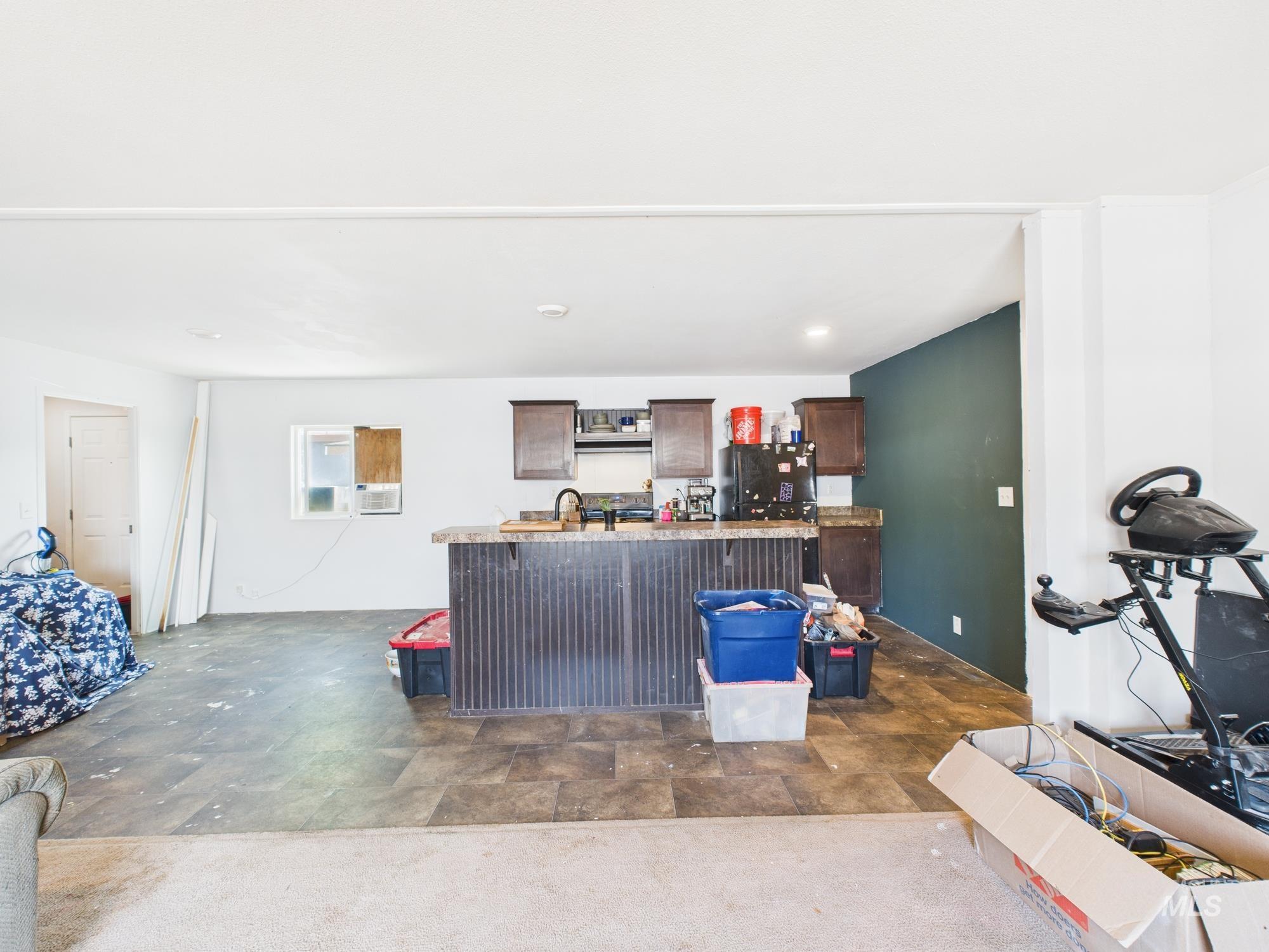 Kitchen featuring dark brown cabinets, light countertops, a kitchen island with sink, and freestanding refrigerator
