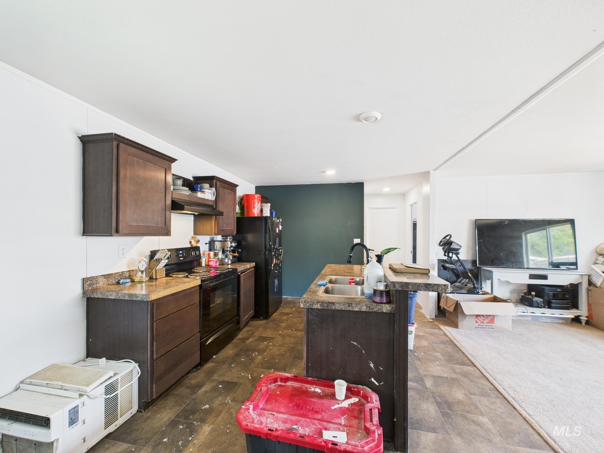 Kitchen with dark brown cabinets, an island with sink, black electric range oven, open floor plan, and a breakfast bar