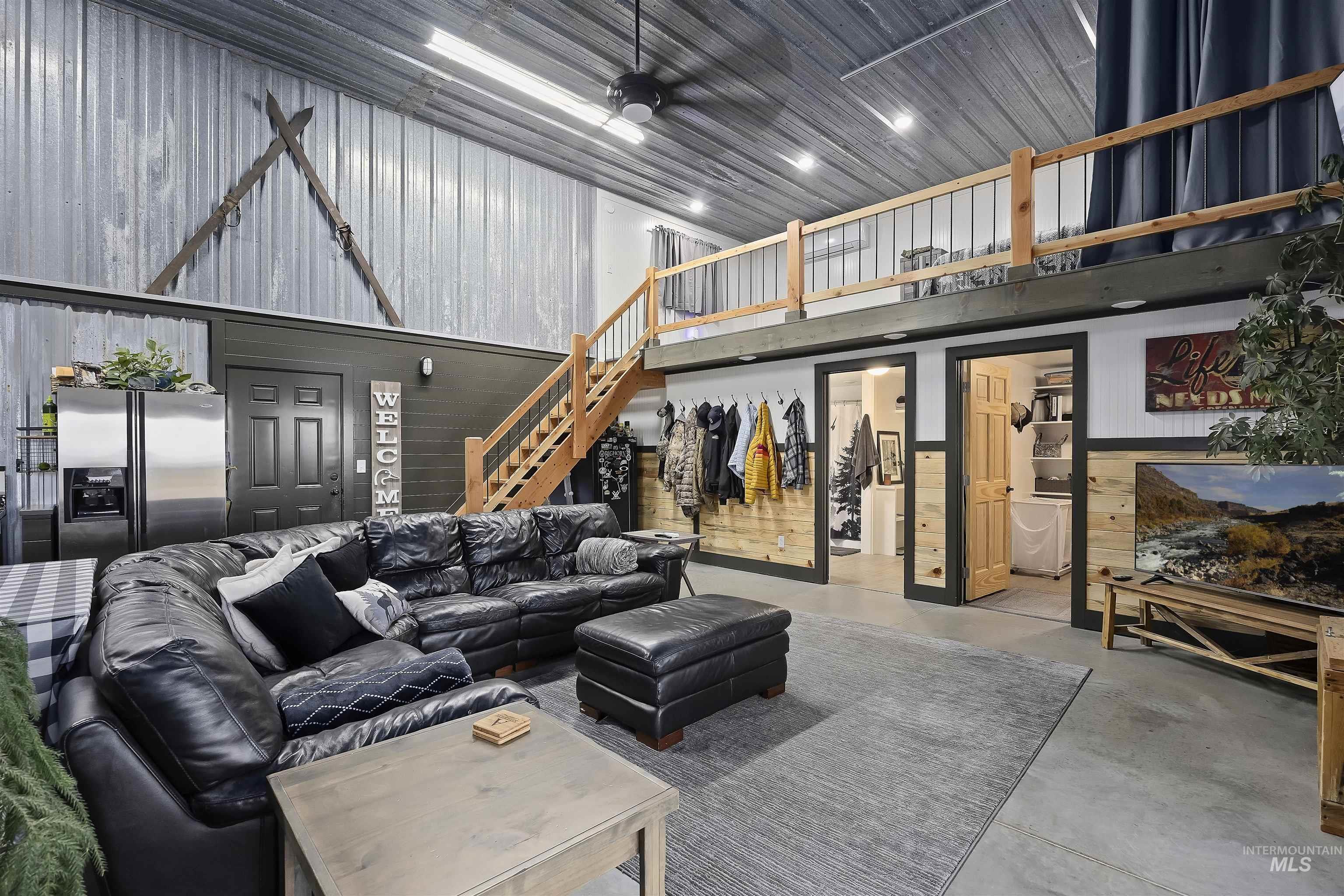 Living area with finished concrete floors, a towering ceiling, stairs, ceiling fan, and wooden walls