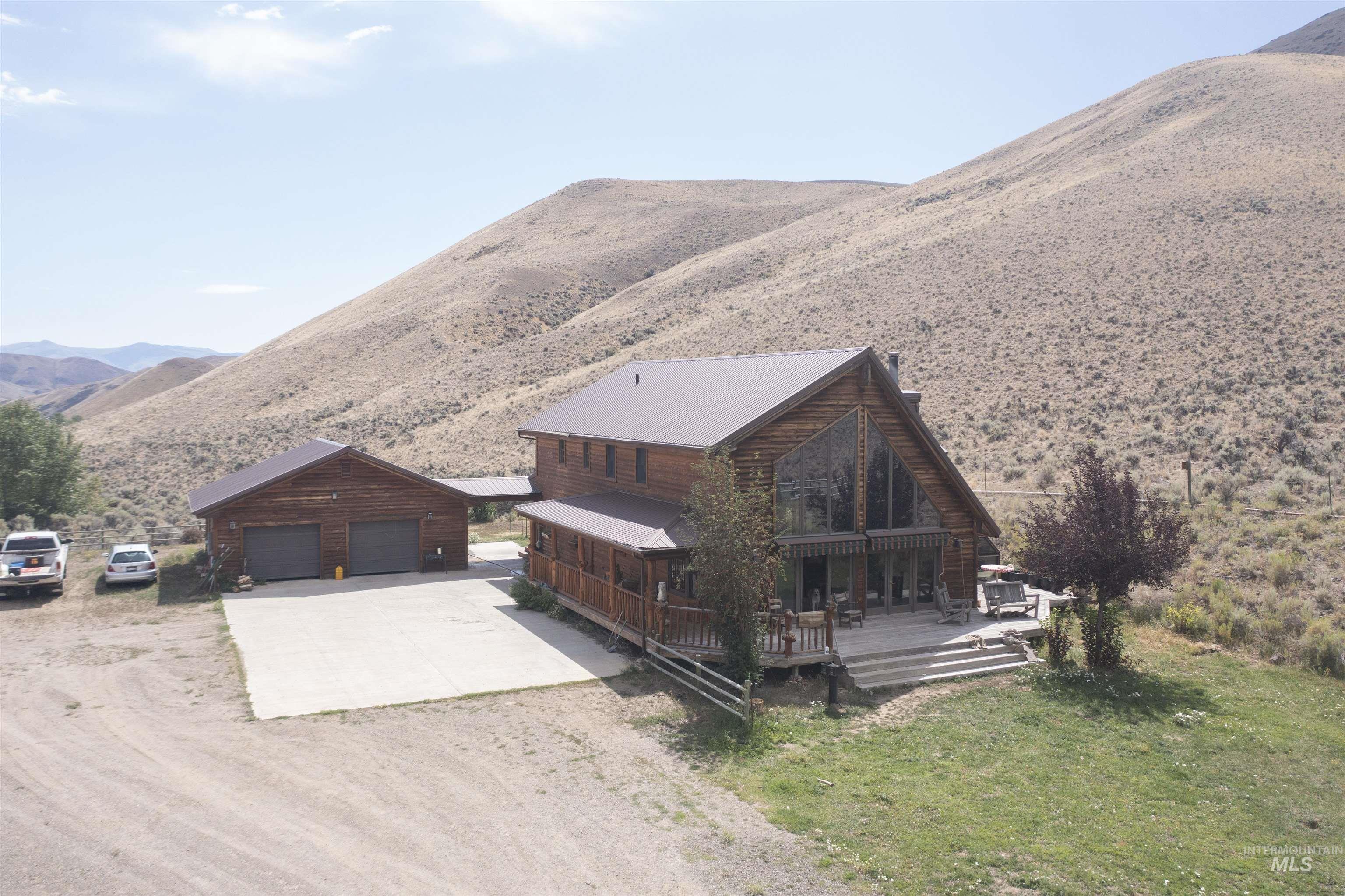 View of front of property with dirt driveway, a deck with mountain view, an outdoor structure, a metal roof, and a front lawn