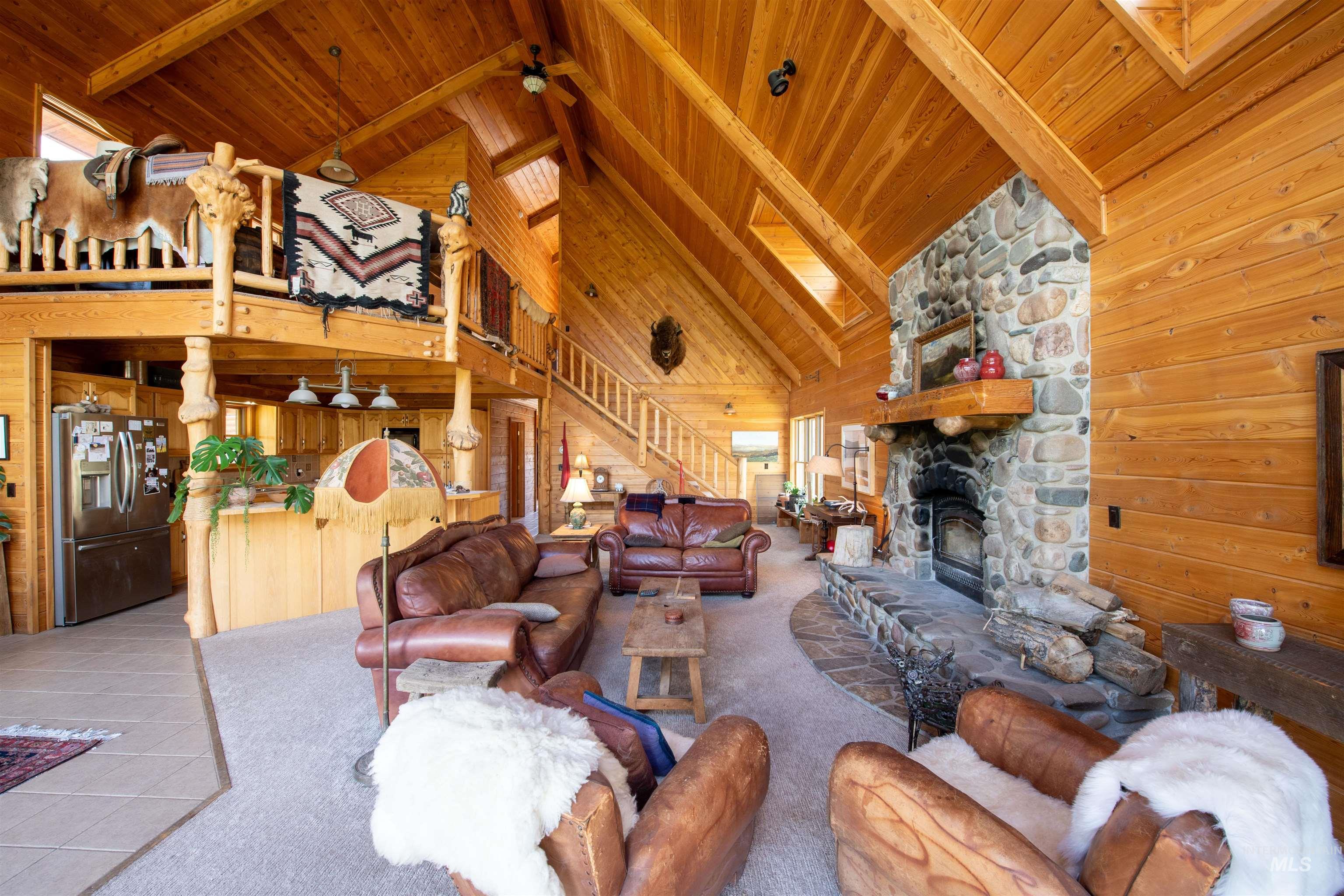 Living area with wood walls, a wooden ceiling with exposed beams, high vaulted ceiling, stairway, and a stone fireplace