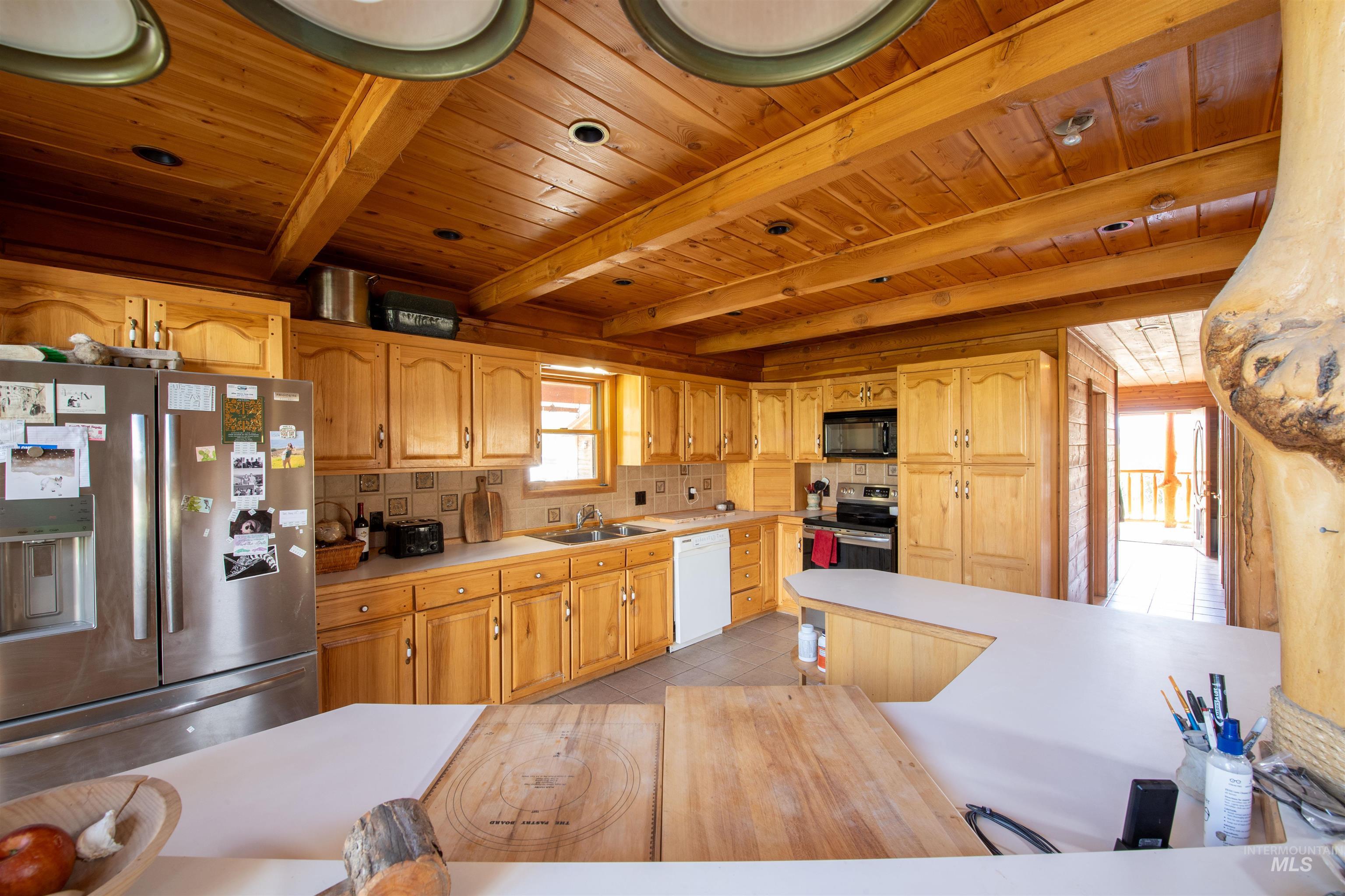 Kitchen featuring light countertops, stainless steel appliances, backsplash, a wood ceiling with exposed beams, and light tile patterned floors
