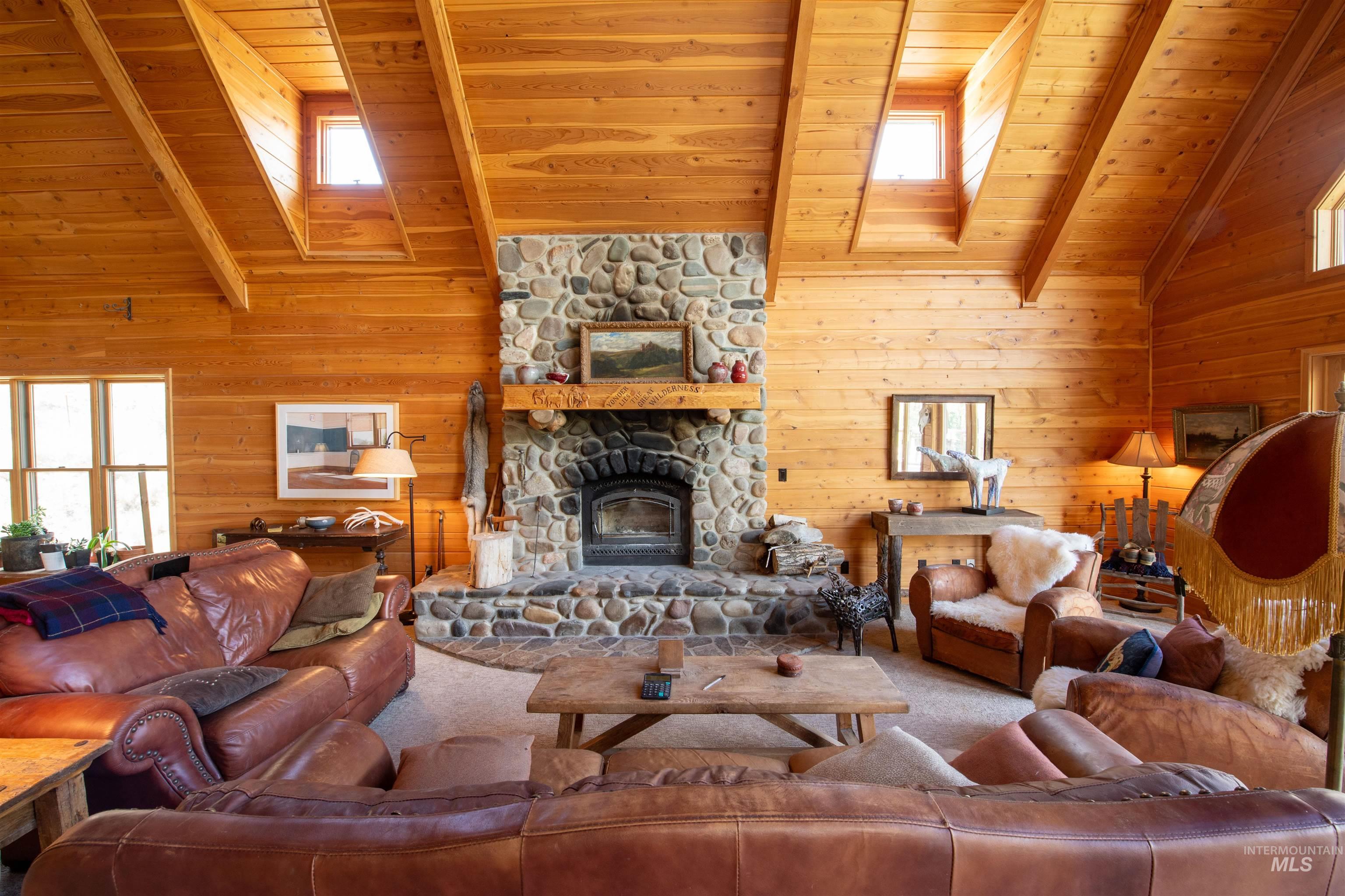 Carpeted living room featuring a stone fireplace, a skylight, a wood ceiling with exposed beams, wooden walls, and high vaulted ceiling