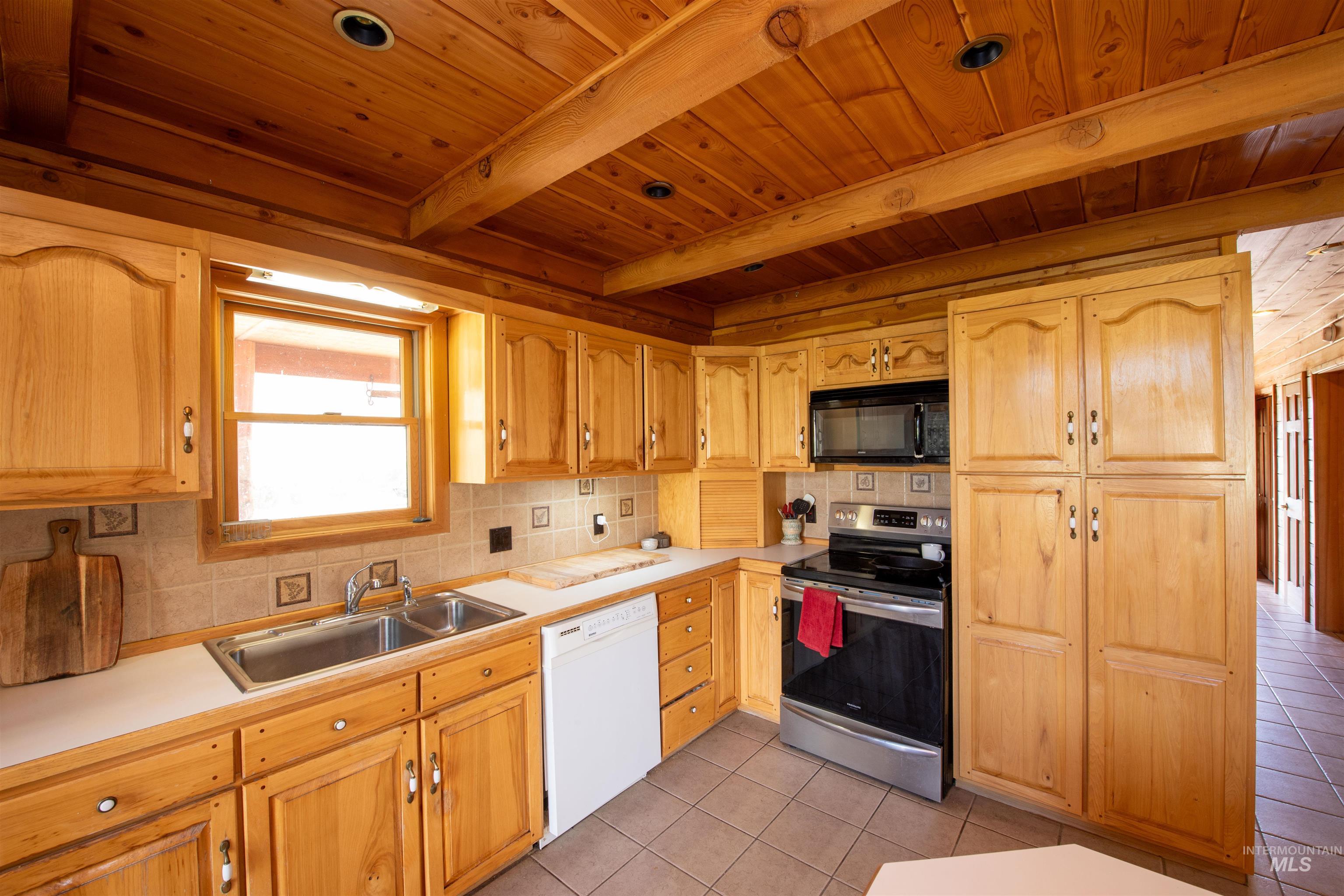Kitchen featuring stainless steel range with electric stovetop, light countertops, backsplash, light tile patterned floors, and black microwave