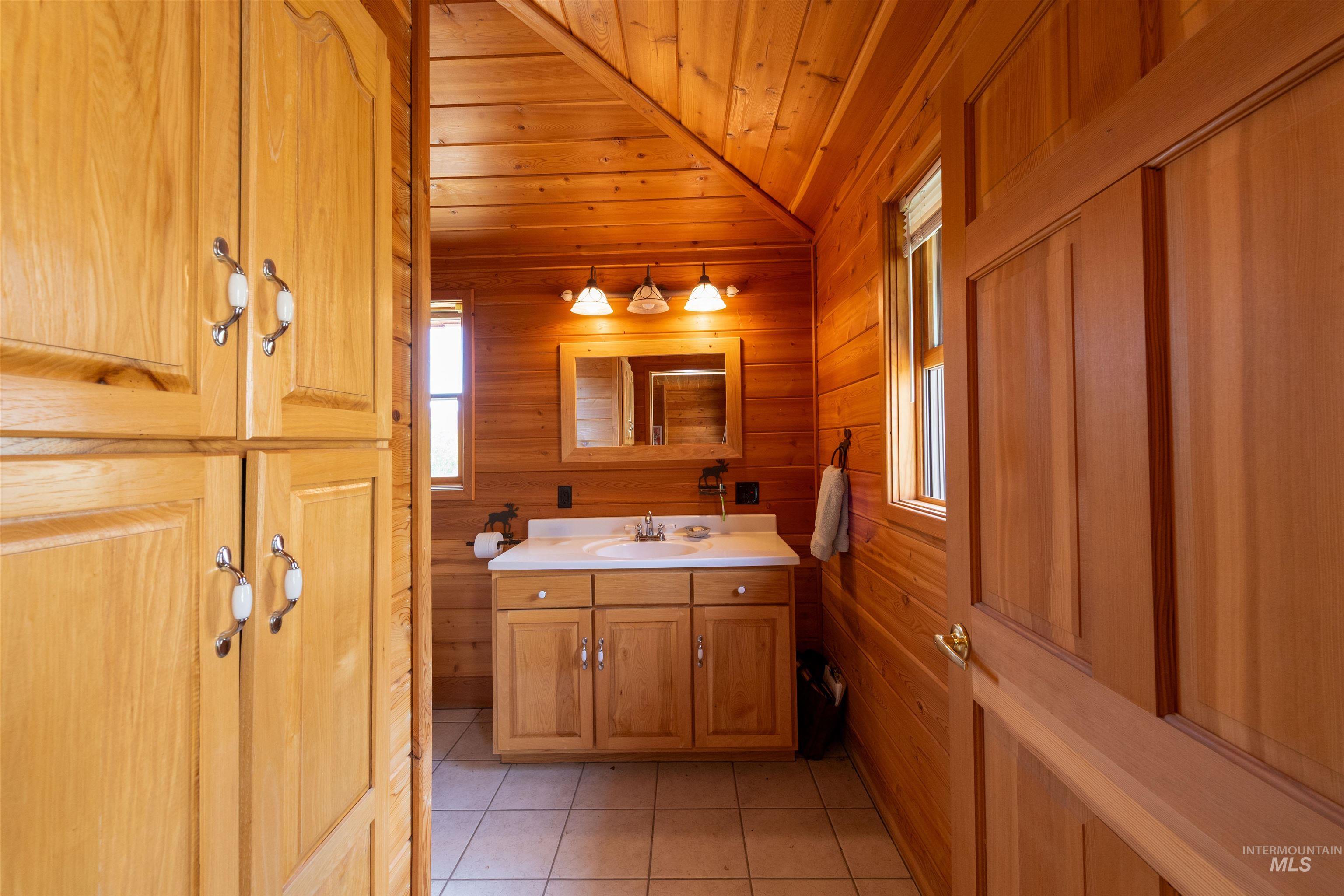 Bathroom featuring light tile patterned floors, wooden walls, vanity, wood ceiling, and vaulted ceiling