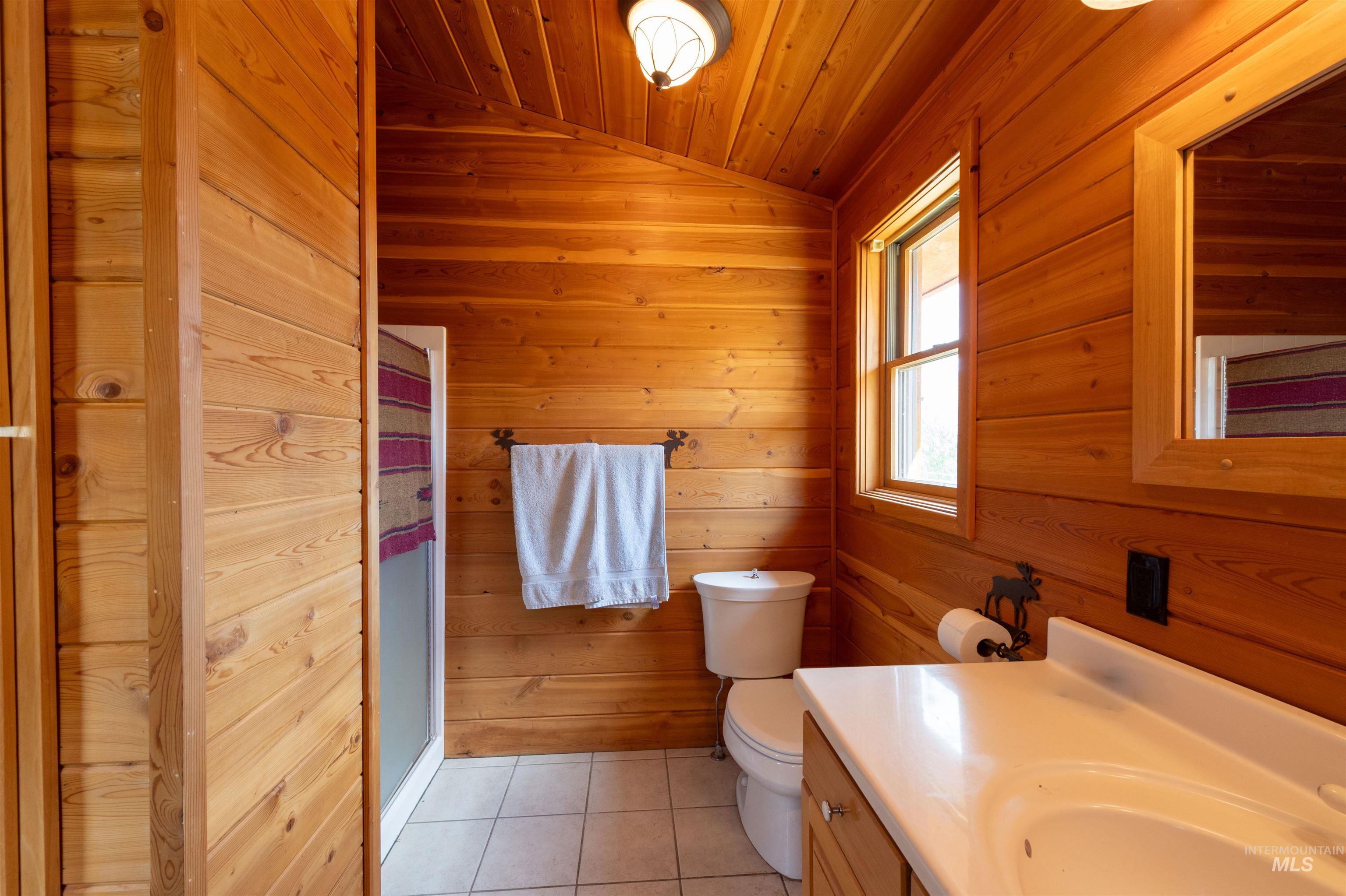 Bathroom featuring light tile patterned floors, vaulted ceiling, wood walls, vanity, and wood ceiling