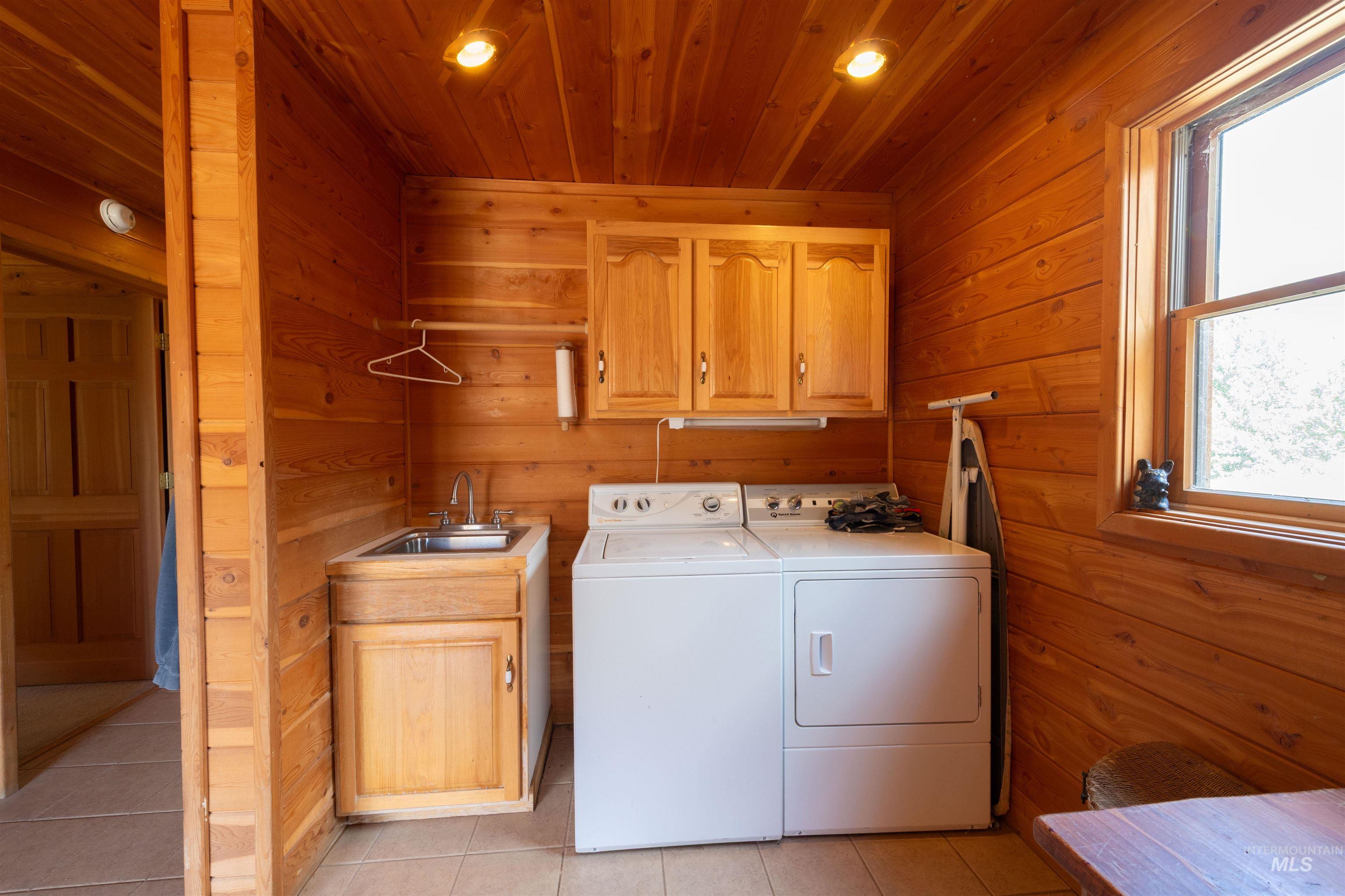 Washroom featuring light tile patterned flooring, wood walls, cabinet space, washer and dryer, and recessed lighting