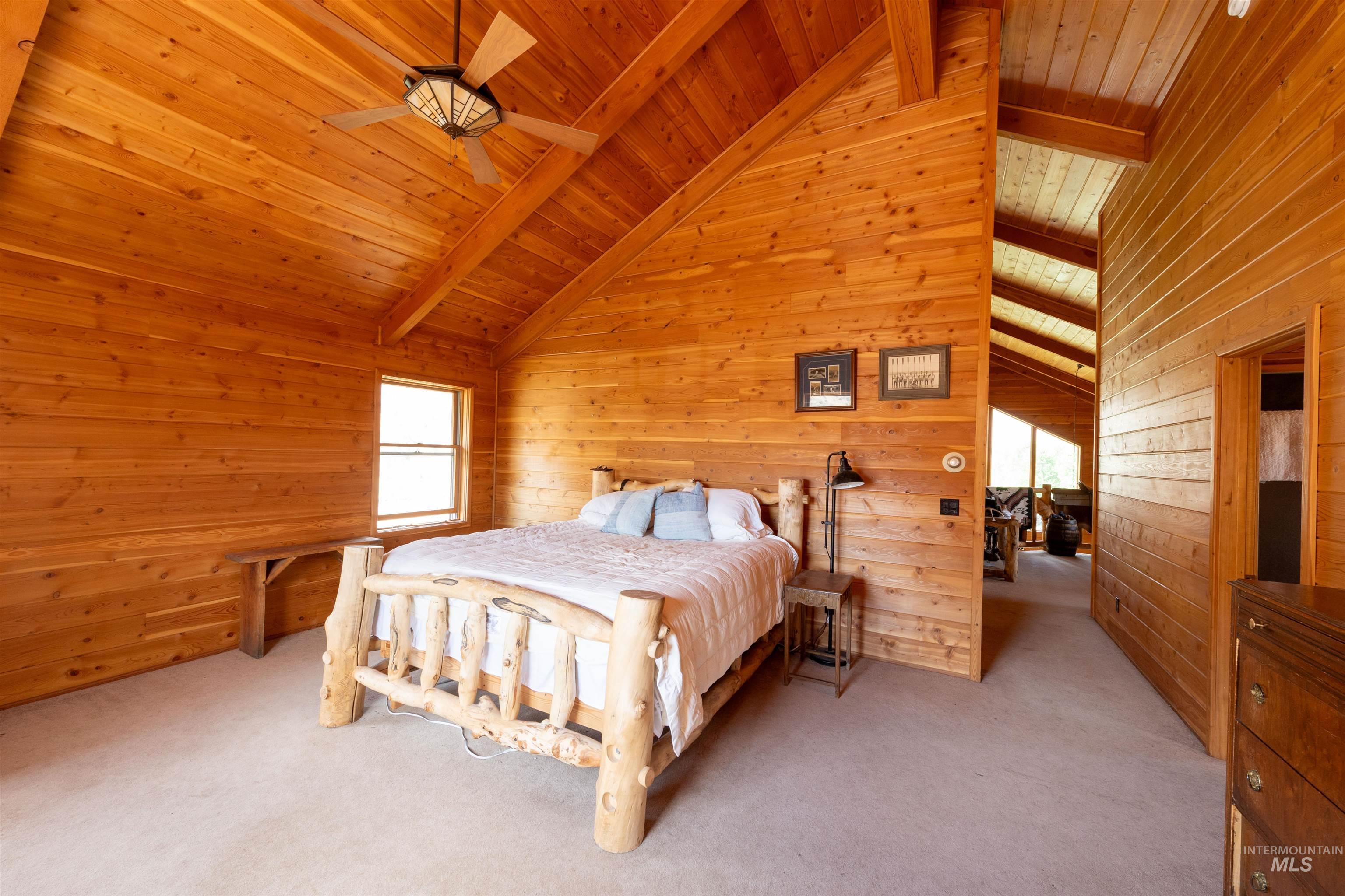 Bedroom with a ceiling fan, wooden walls, light colored carpet, a wooden ceiling with exposed beams, and high vaulted ceiling