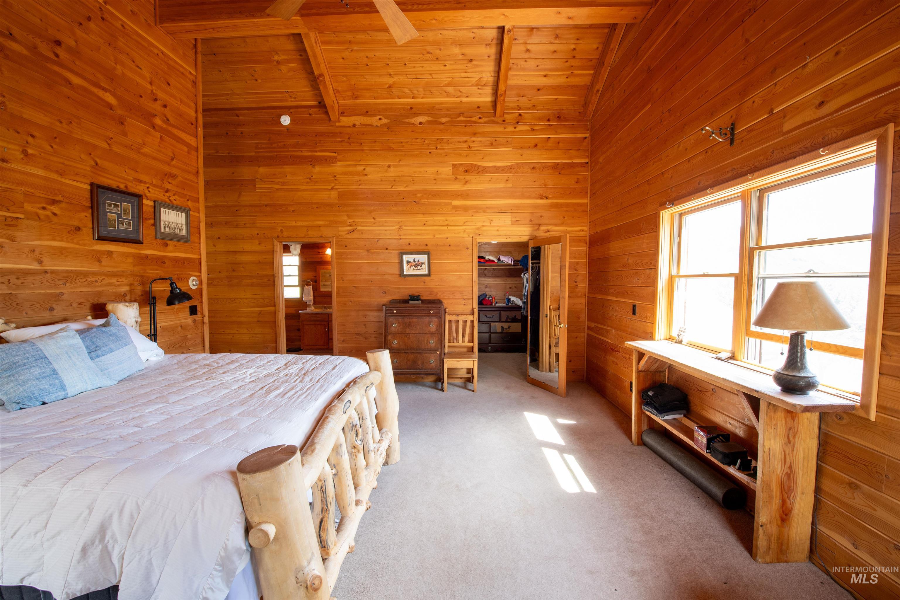 Carpeted bedroom with wood walls, high vaulted ceiling, and a wood ceiling with exposed beams