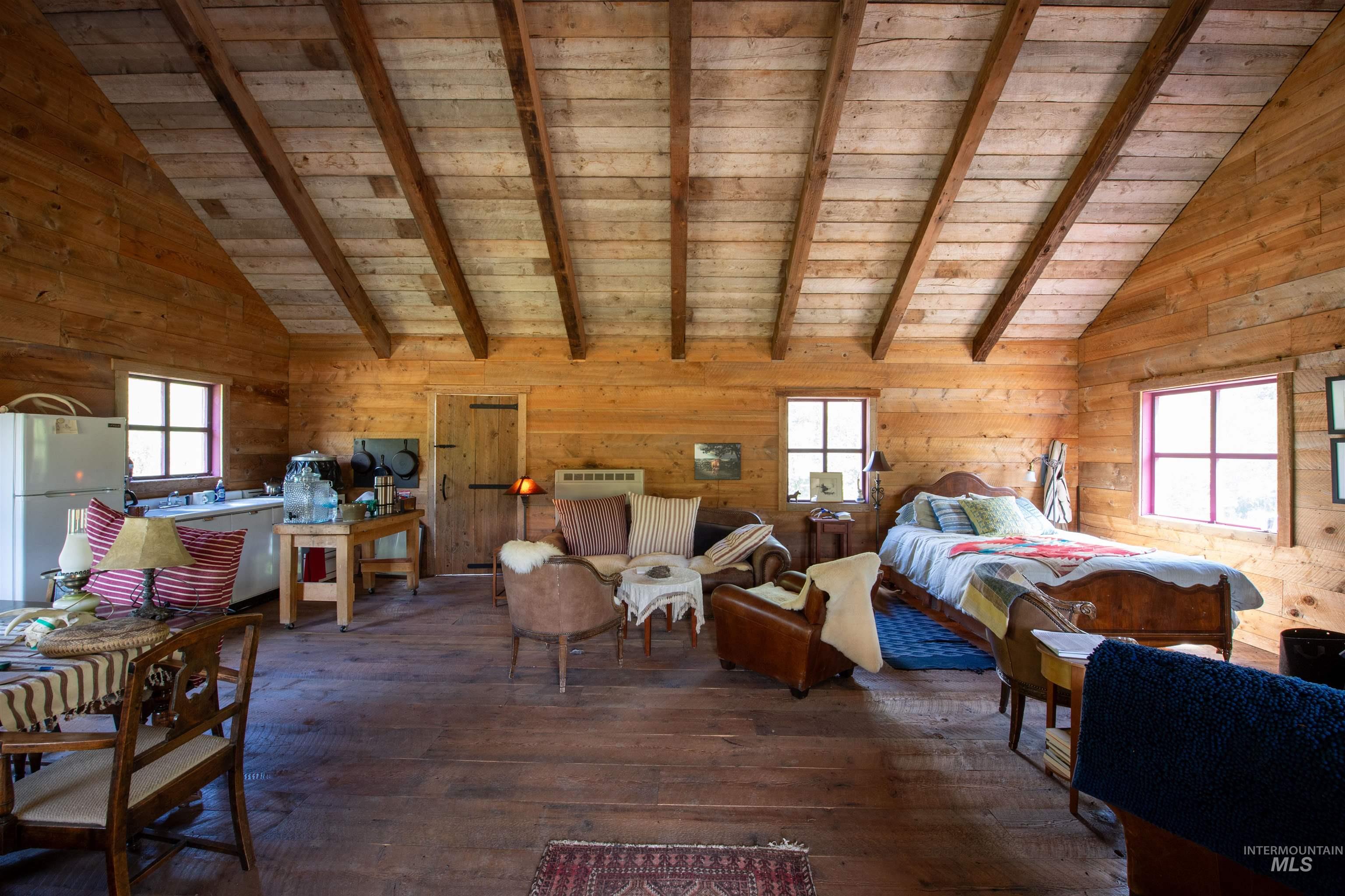 Bedroom featuring wooden walls, freestanding refrigerator, dark wood finished floors, a wooden ceiling with exposed beams, and high vaulted ceiling
