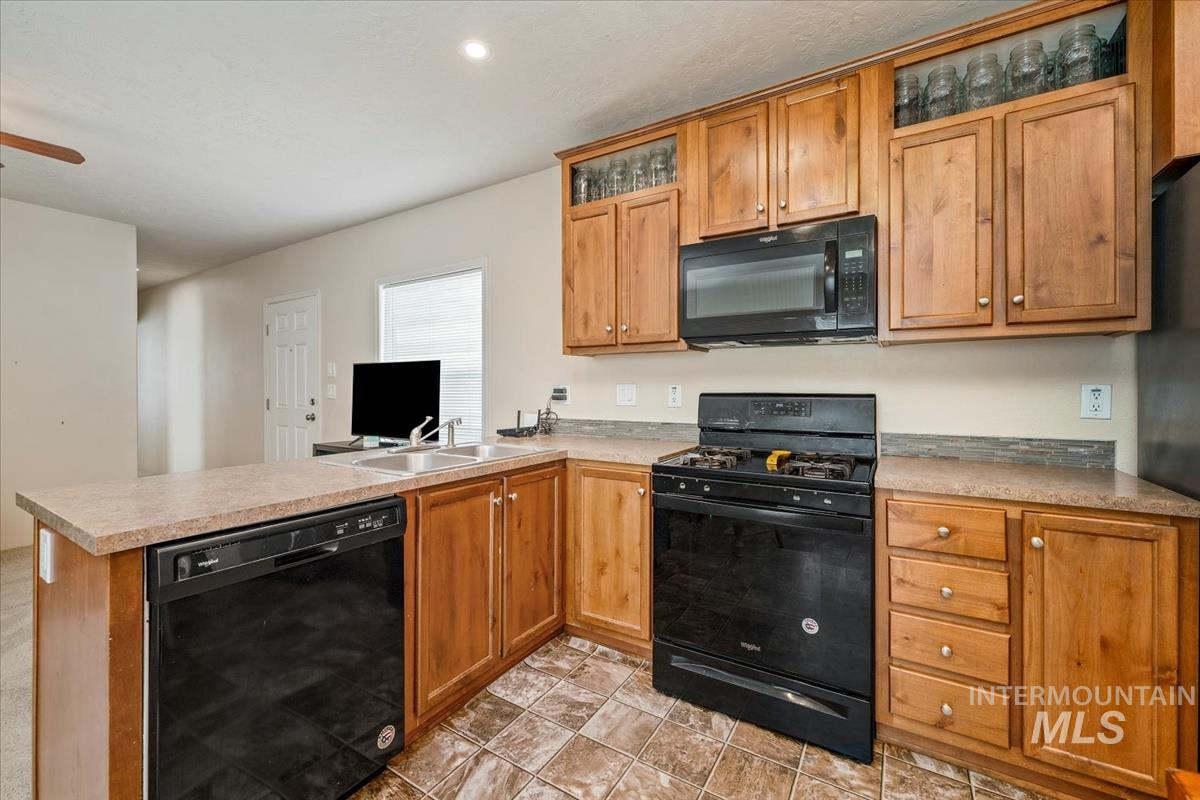 Kitchen with black appliances, brown cabinets, a peninsula, light countertops, and glass insert cabinets