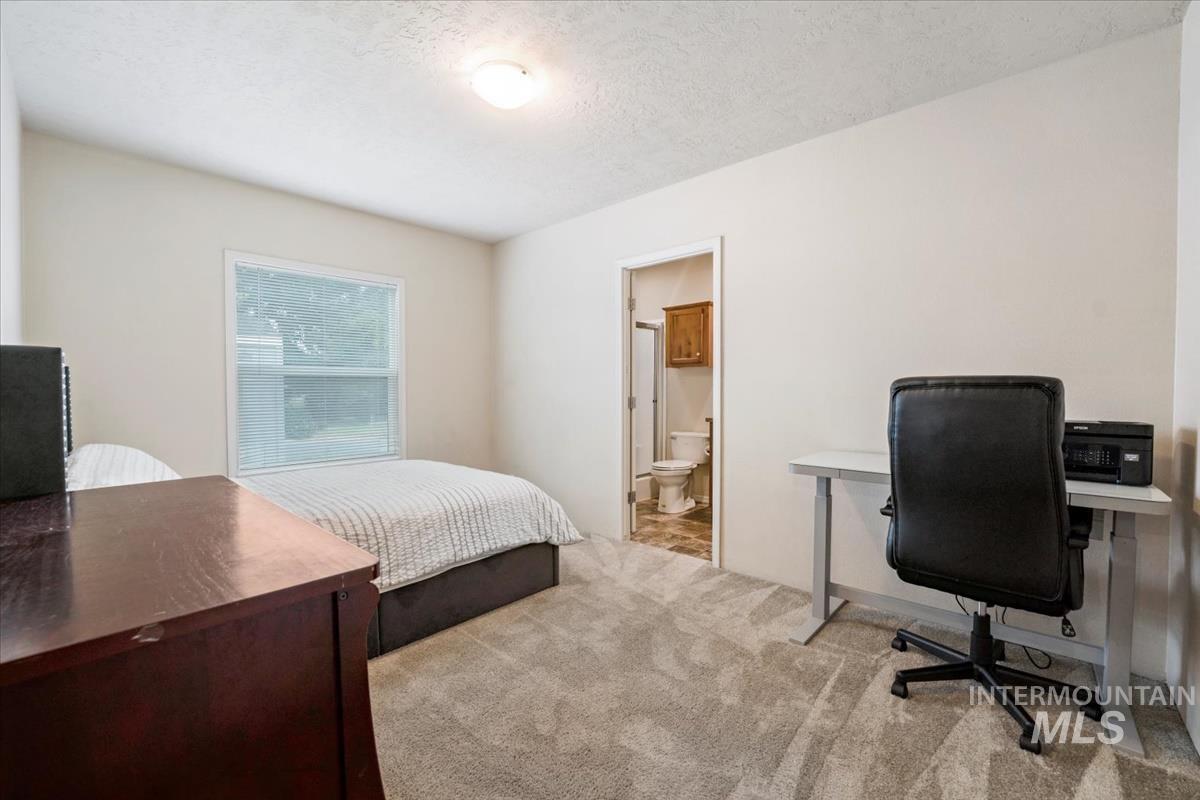 Bedroom featuring light carpet, a desk, a textured ceiling, and connected bathroom