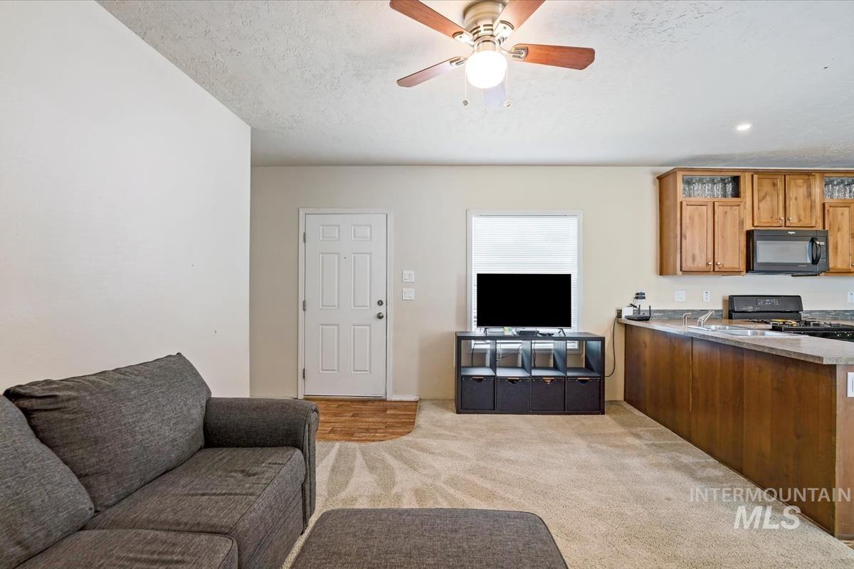 Living room featuring a textured ceiling, light colored carpet, and a ceiling fan