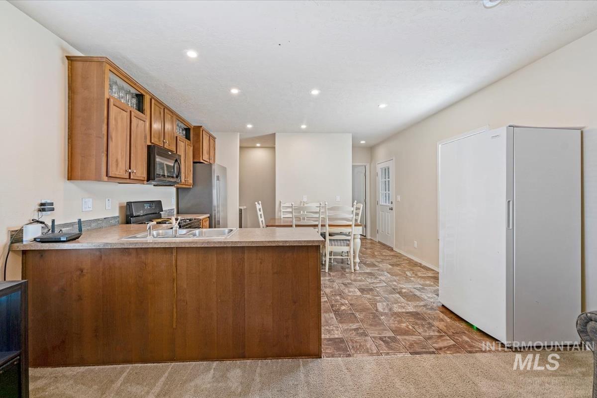 Kitchen with a peninsula, brown cabinetry, black appliances, light countertops, and stone finish floors