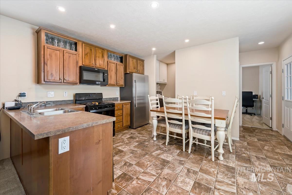 Kitchen featuring brown cabinetry, a peninsula, black appliances, recessed lighting, and light countertops