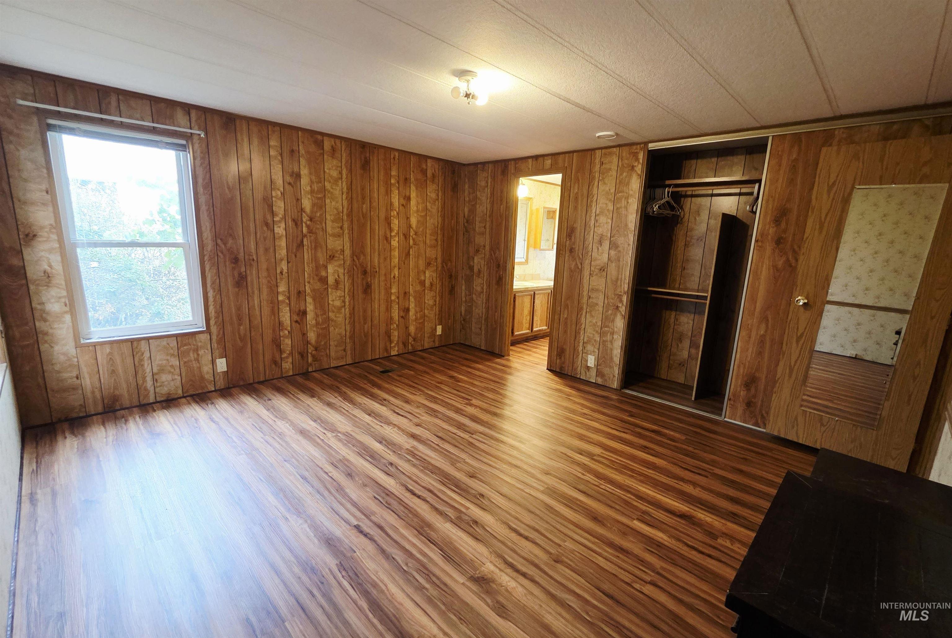 Unfurnished bedroom with wood finished floors, a closet, wood walls, and ensuite bathroom