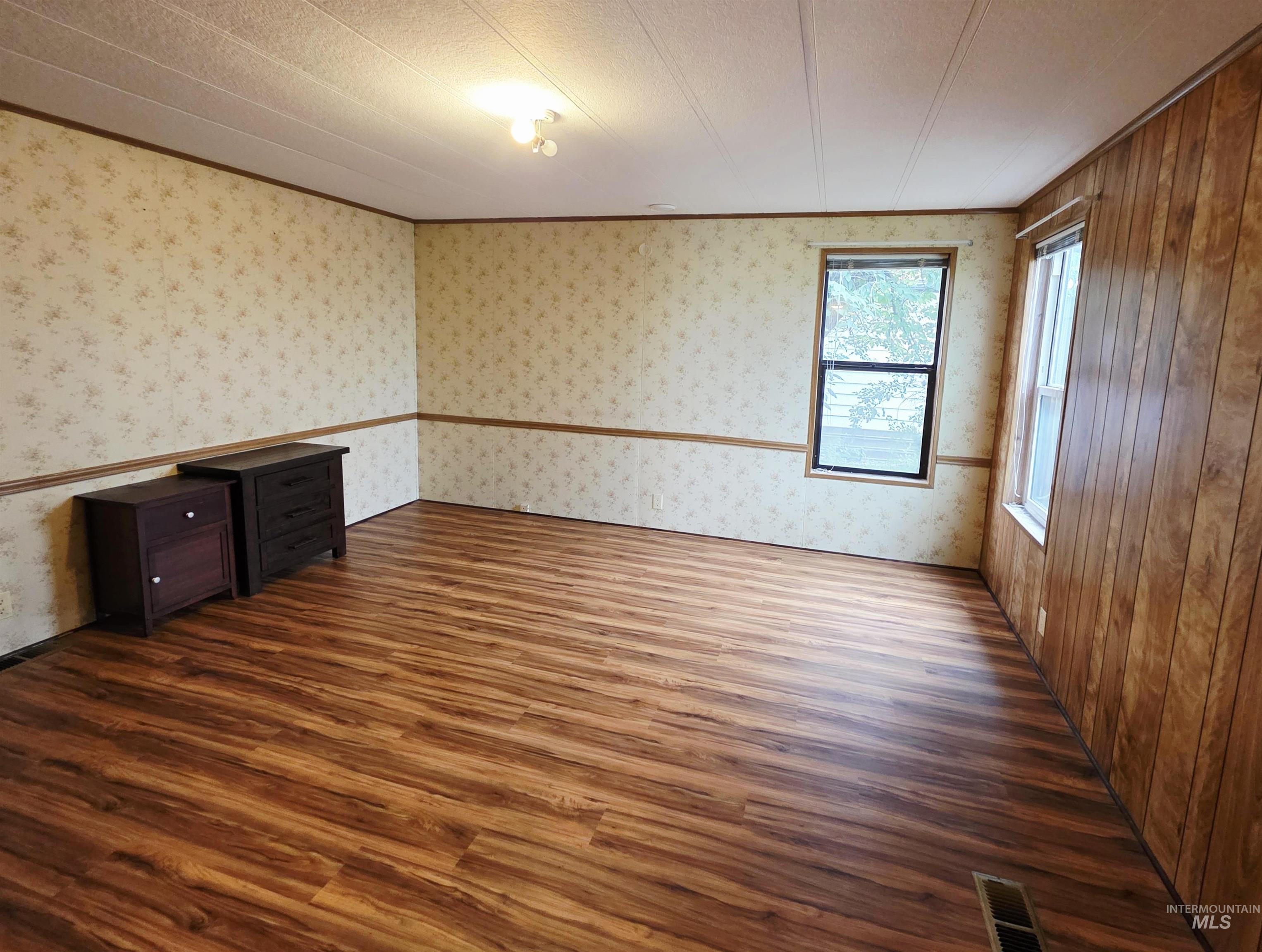 Empty room with ornamental molding, dark wood finished floors, wallpapered walls, and a textured ceiling