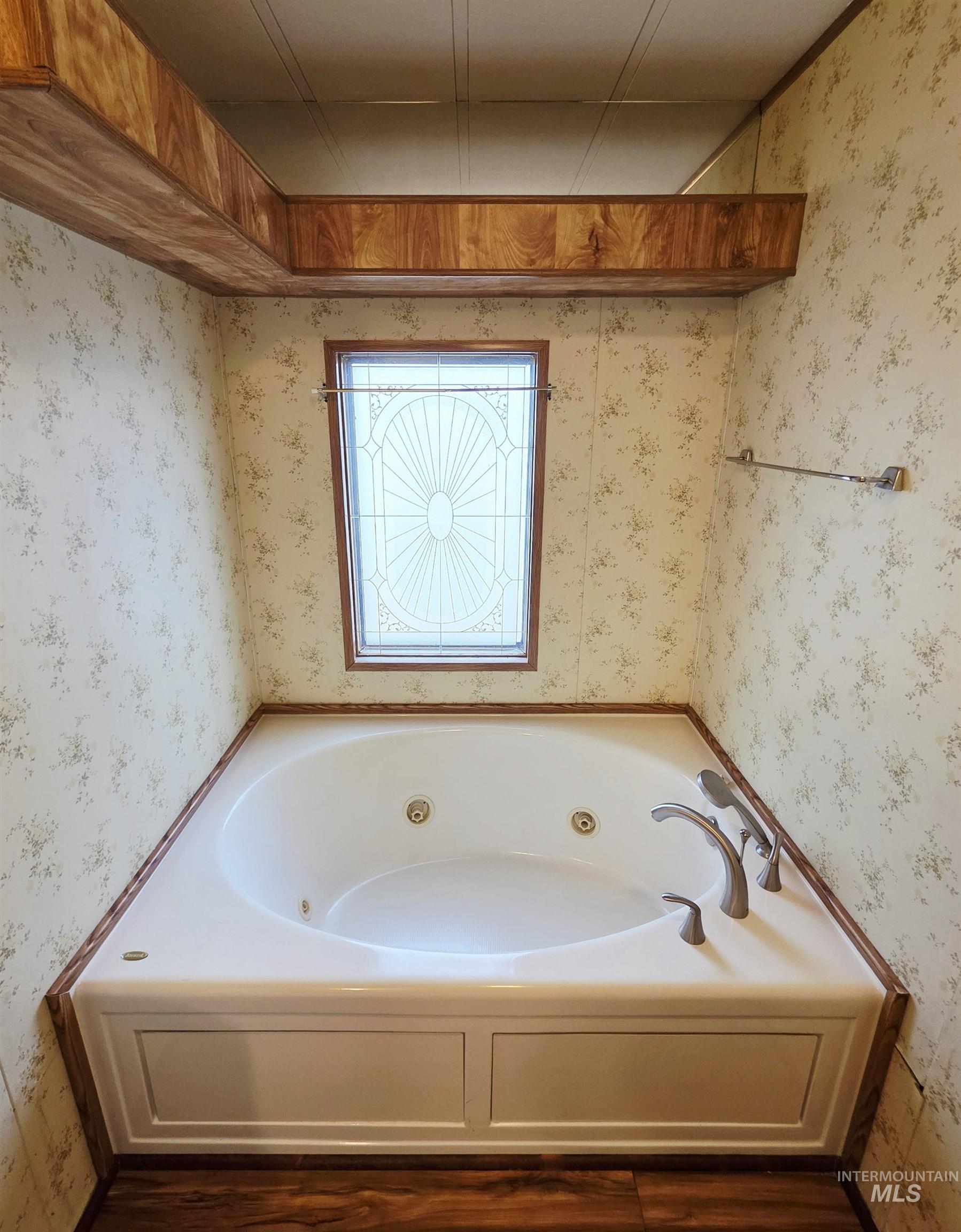 Bathroom featuring a tub with jets, wallpapered walls, and dark wood finished floors