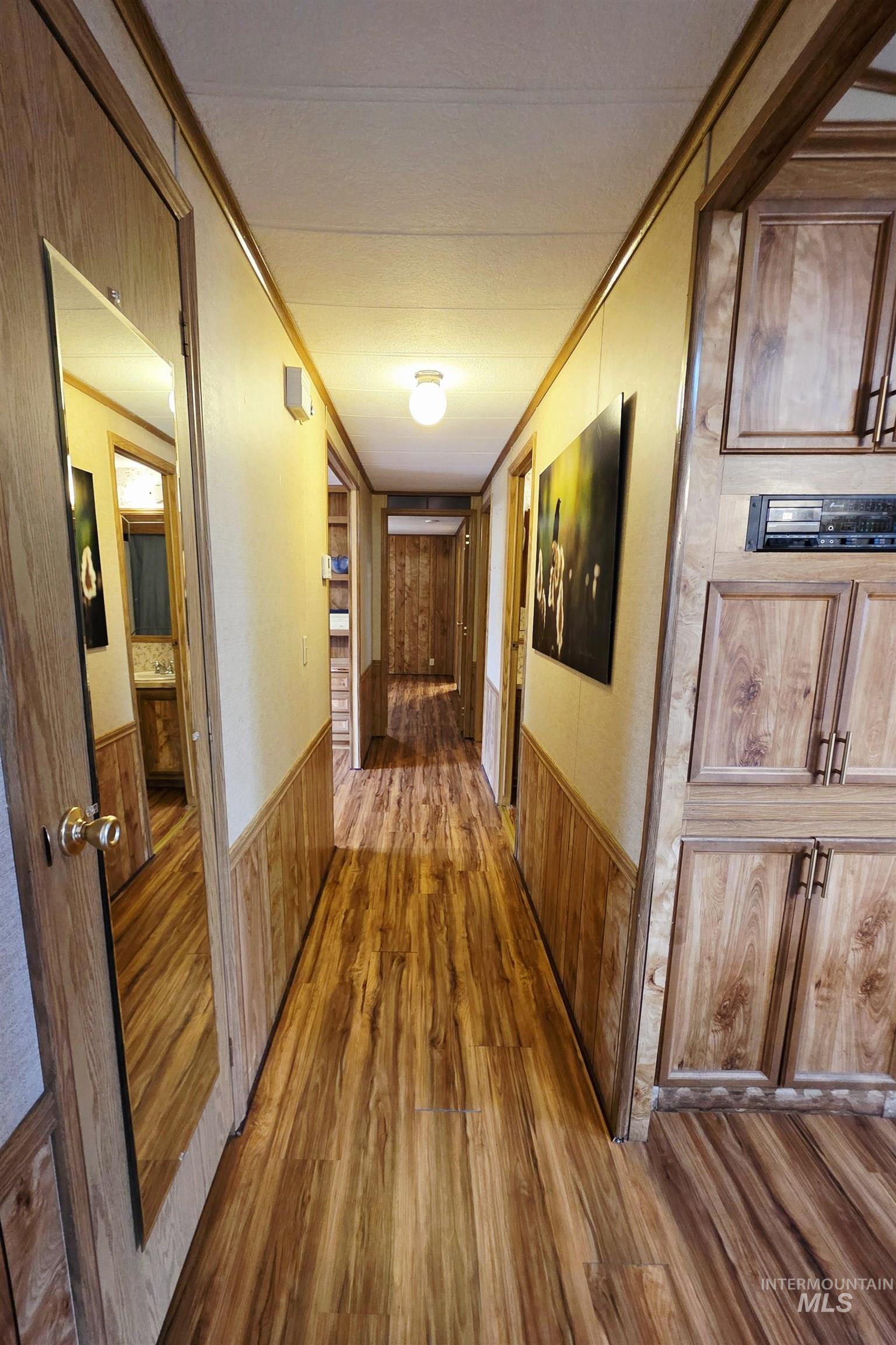 Hall featuring wood finished floors, crown molding, wainscoting, and wood walls