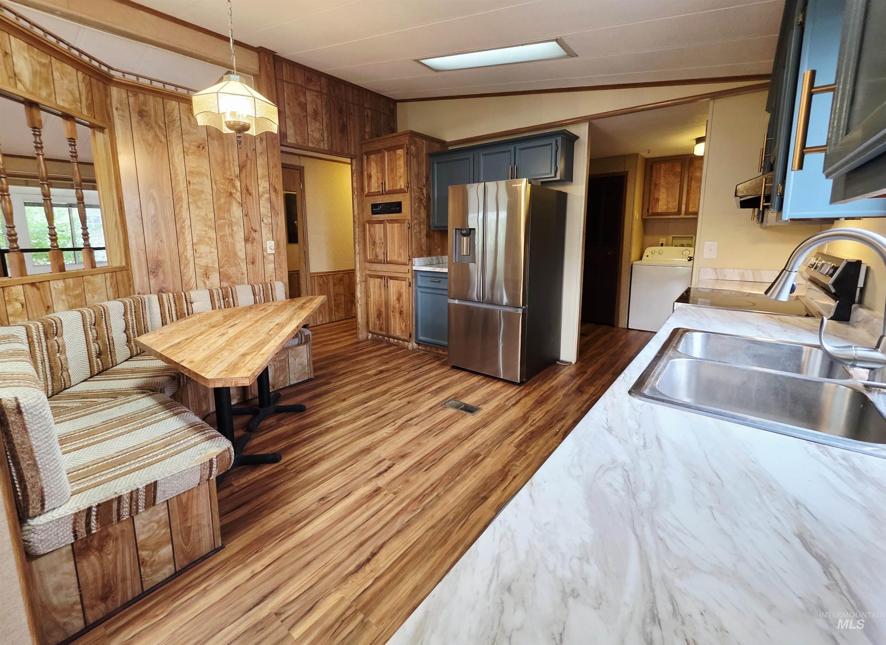 Kitchen with wooden walls, stainless steel fridge with ice dispenser, light countertops, hanging light fixtures, and washer / dryer