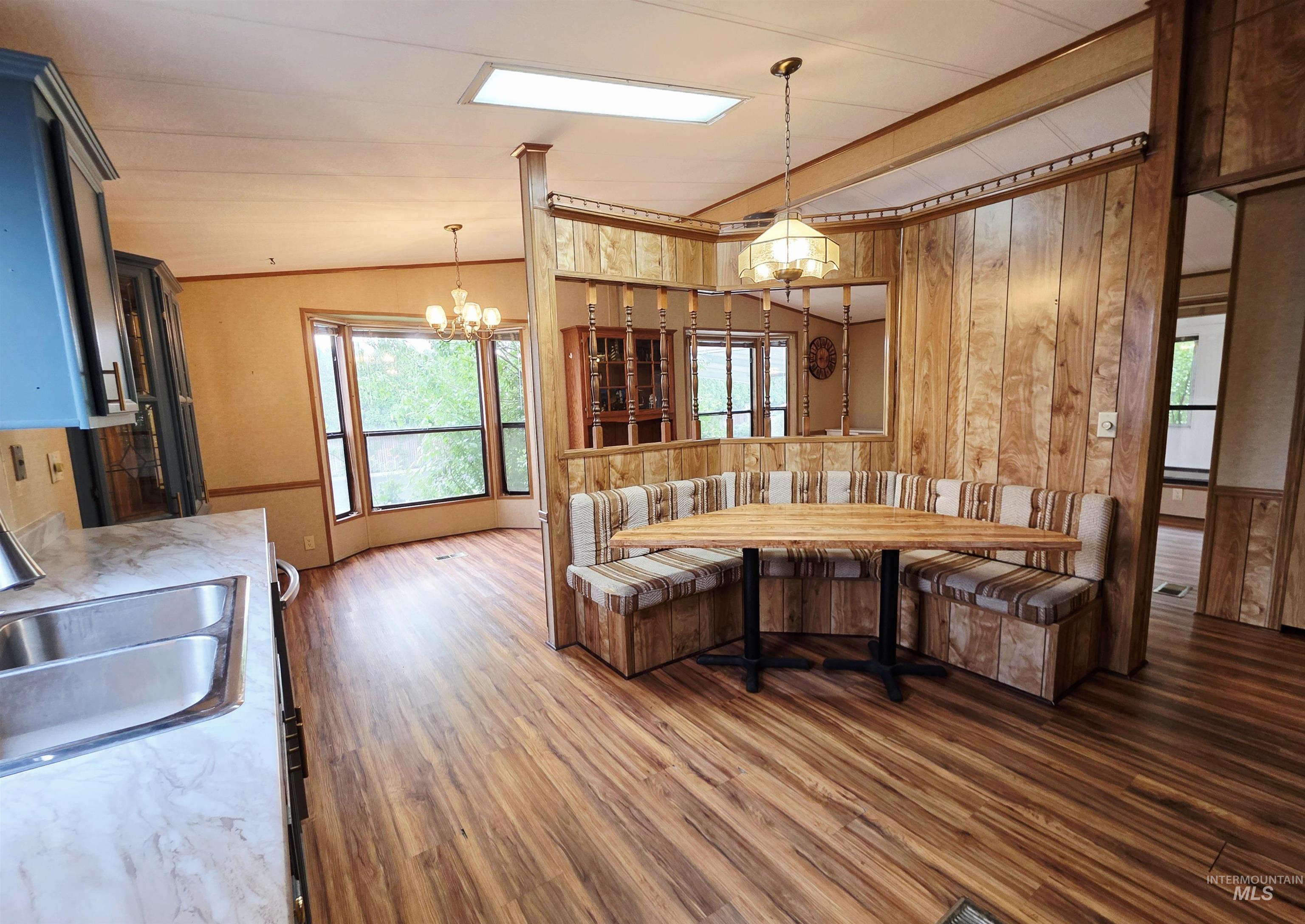 Kitchen featuring wood finished floors, a chandelier, hanging light fixtures, wooden walls, and light countertops