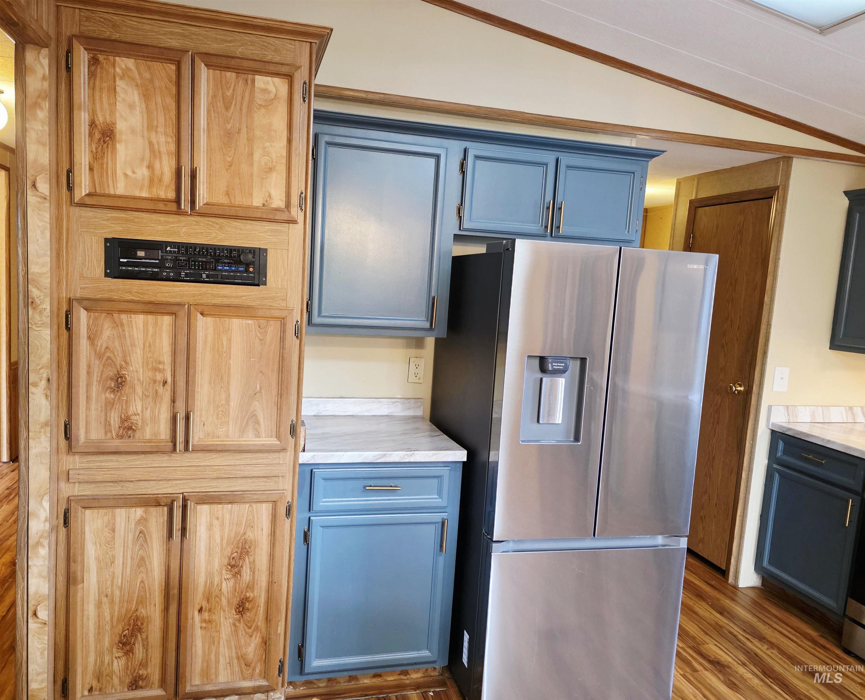 Kitchen featuring stainless steel refrigerator with ice dispenser, light countertops, lofted ceiling, dark wood-style flooring, and blue cabinets