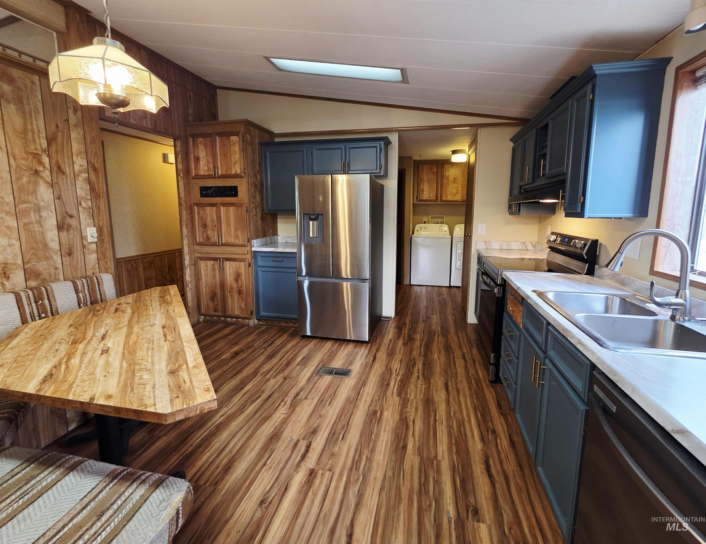 Kitchen featuring vaulted ceiling, wood walls, light countertops, blue cabinets, and appliances with stainless steel finishes