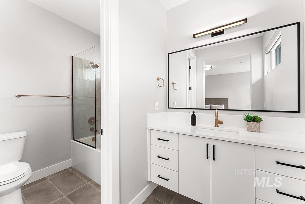 Bathroom with dark tile patterned flooring, vanity, and bath / shower combo with glass door