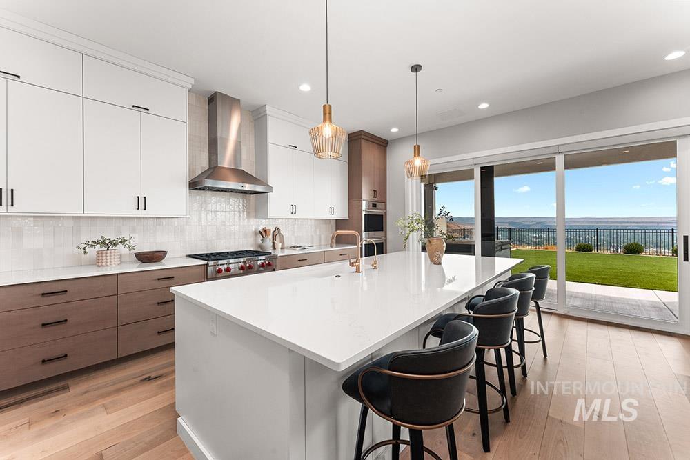 Kitchen featuring white cabinets, backsplash, pendant lighting, light wood-type flooring, and a kitchen island with sink