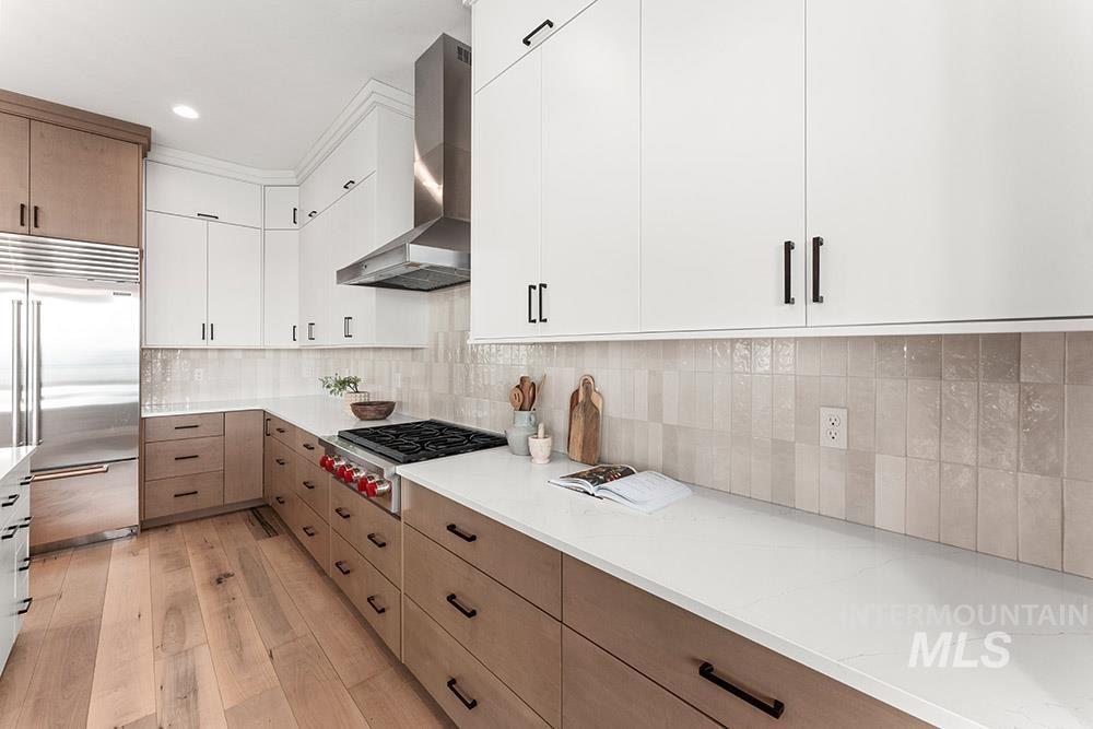 Kitchen featuring modern cabinets, white cabinets, stainless steel appliances, wall chimney range hood, and backsplash